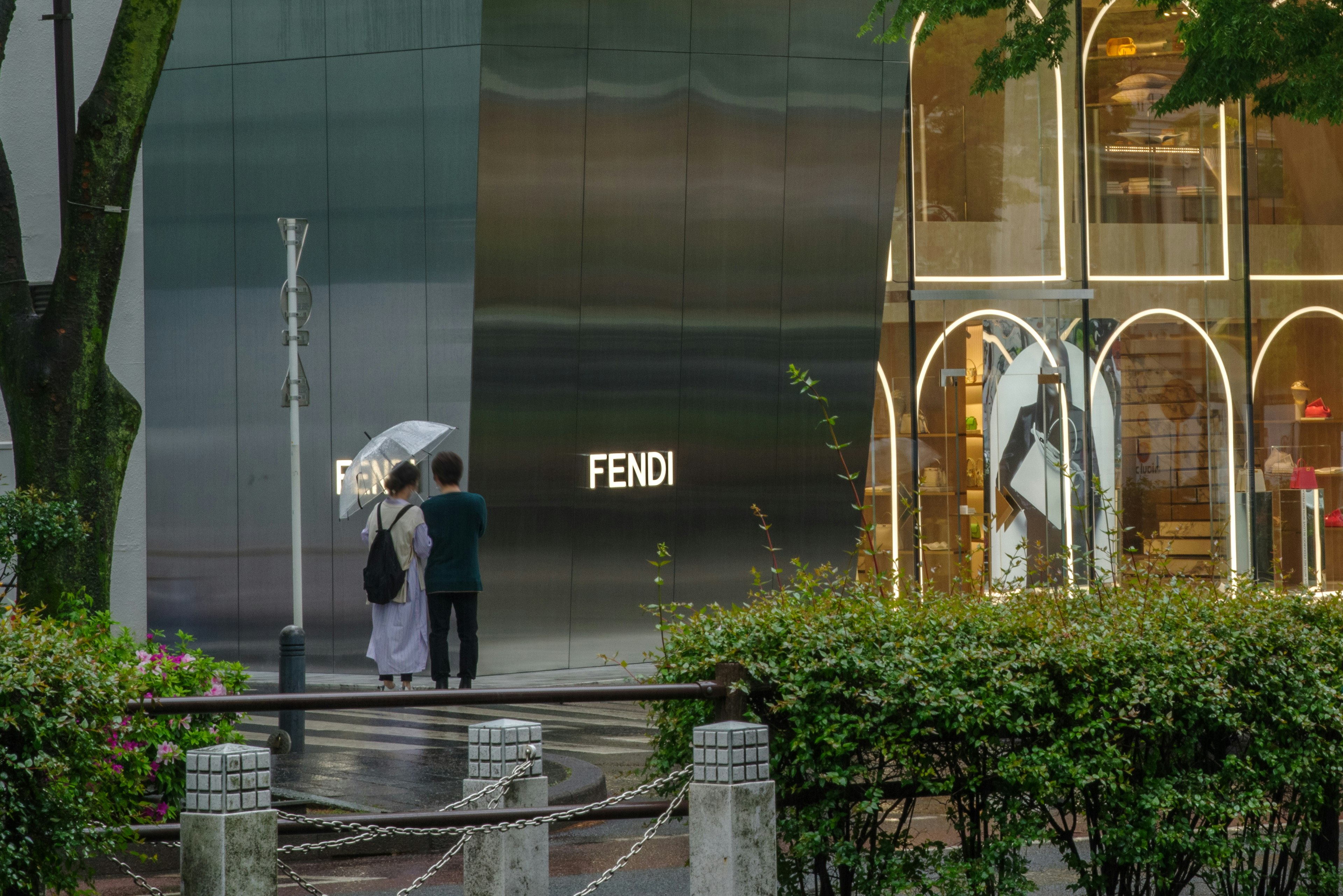 A couple holding an umbrella stands in front of a FENDI store in the rain