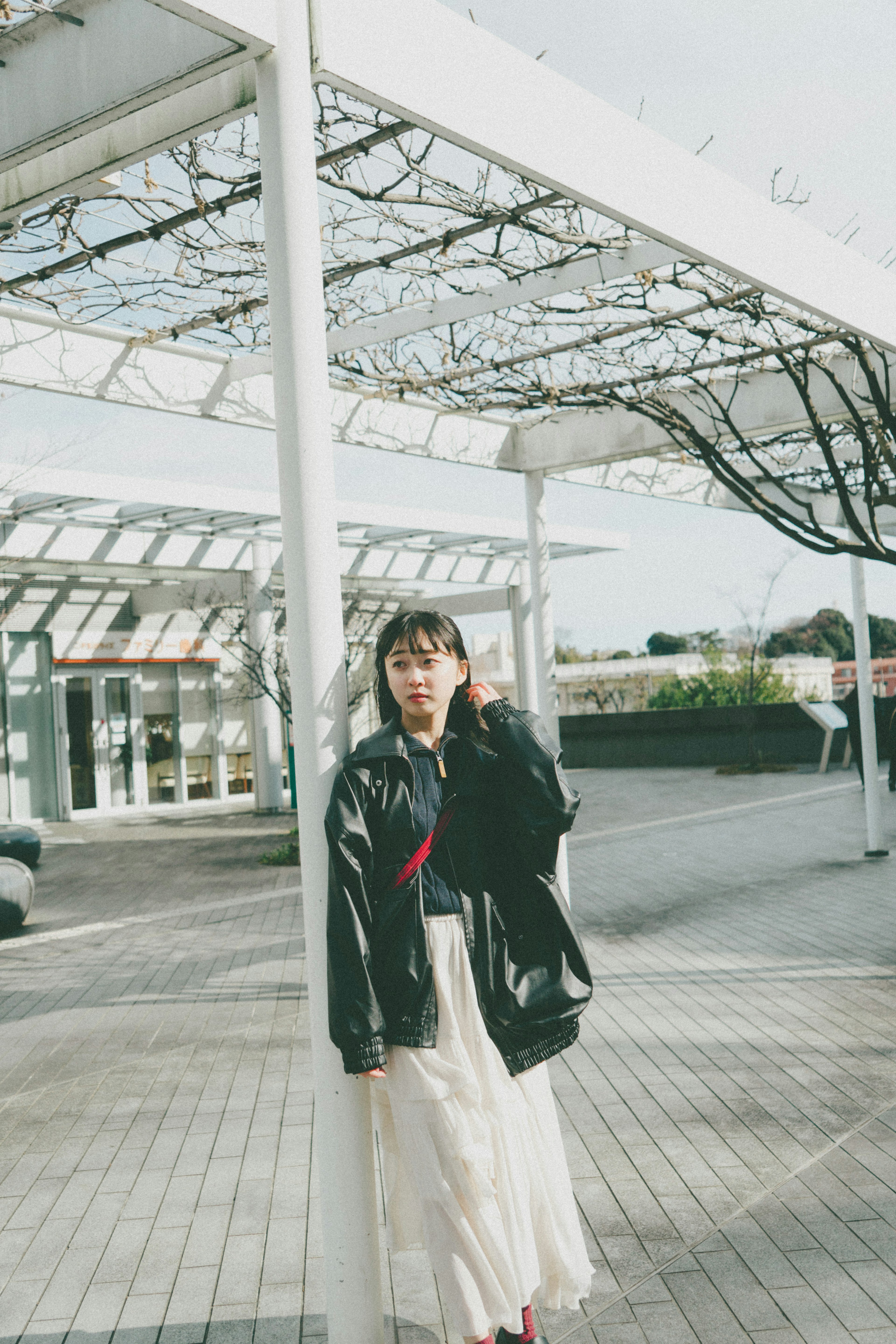 A woman wearing a black jacket and a white skirt in an outdoor setting