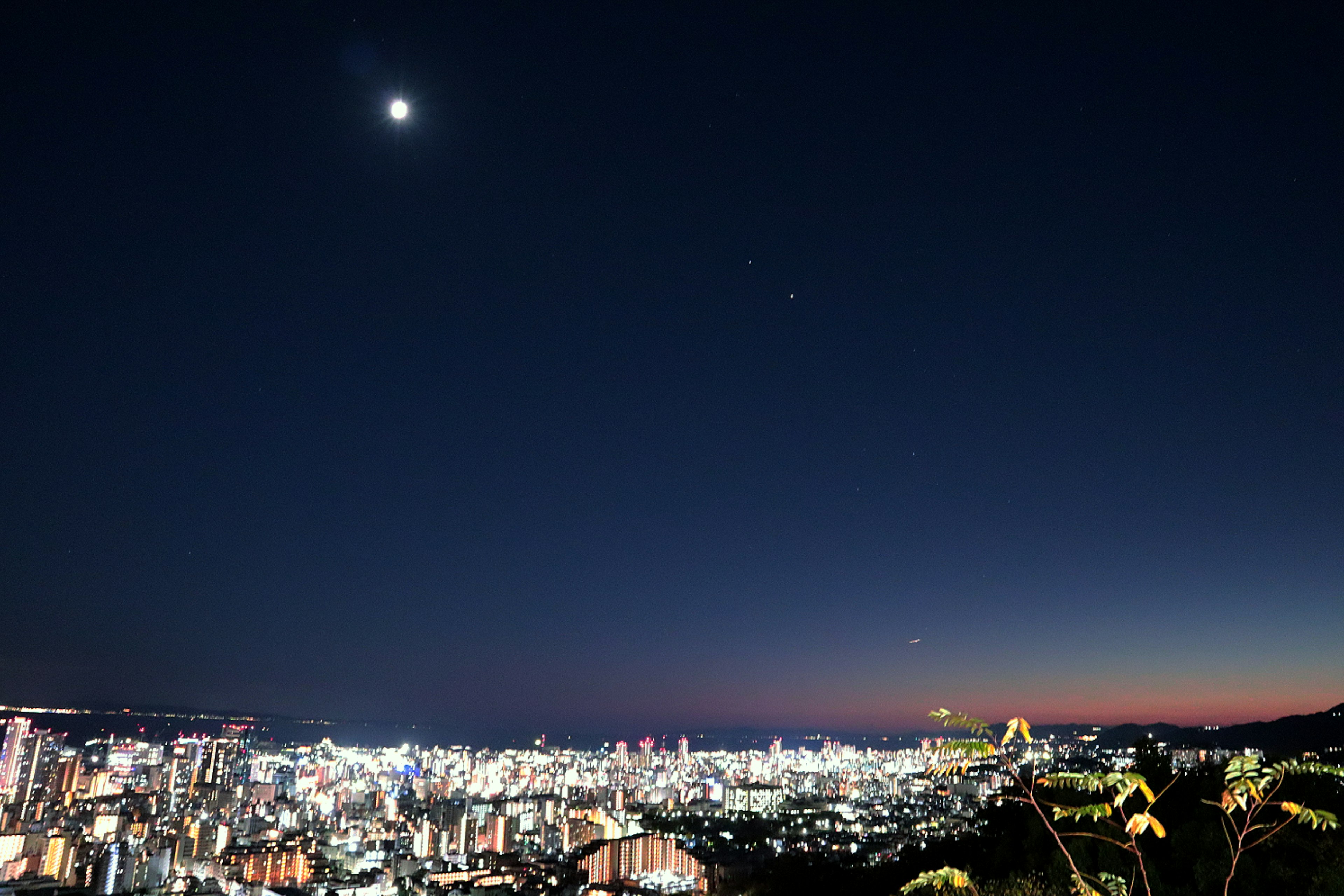 Cityscape at night with bright lights and a visible moon