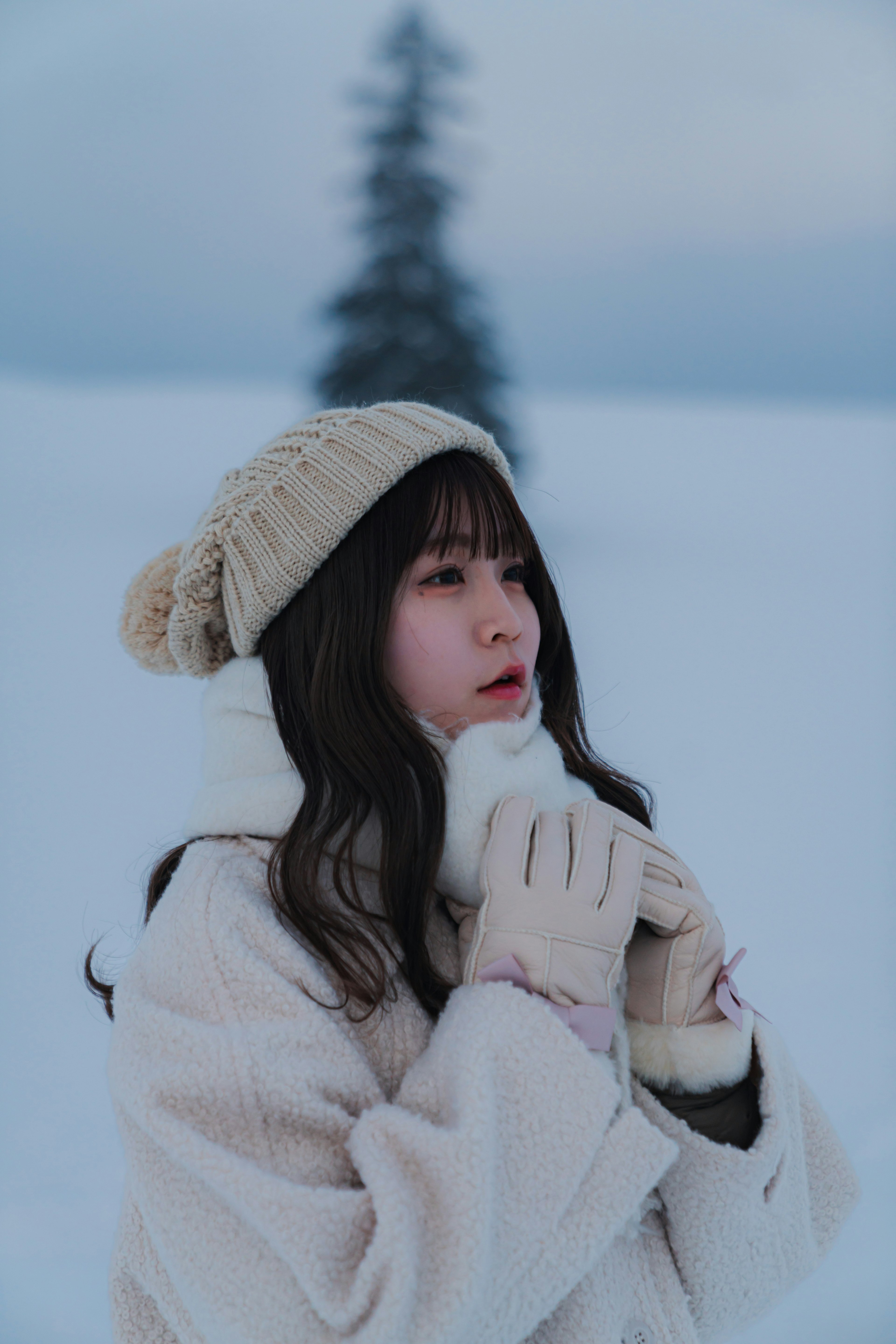 Una mujer con abrigo blanco y gorro de lana calentando sus manos en la nieve