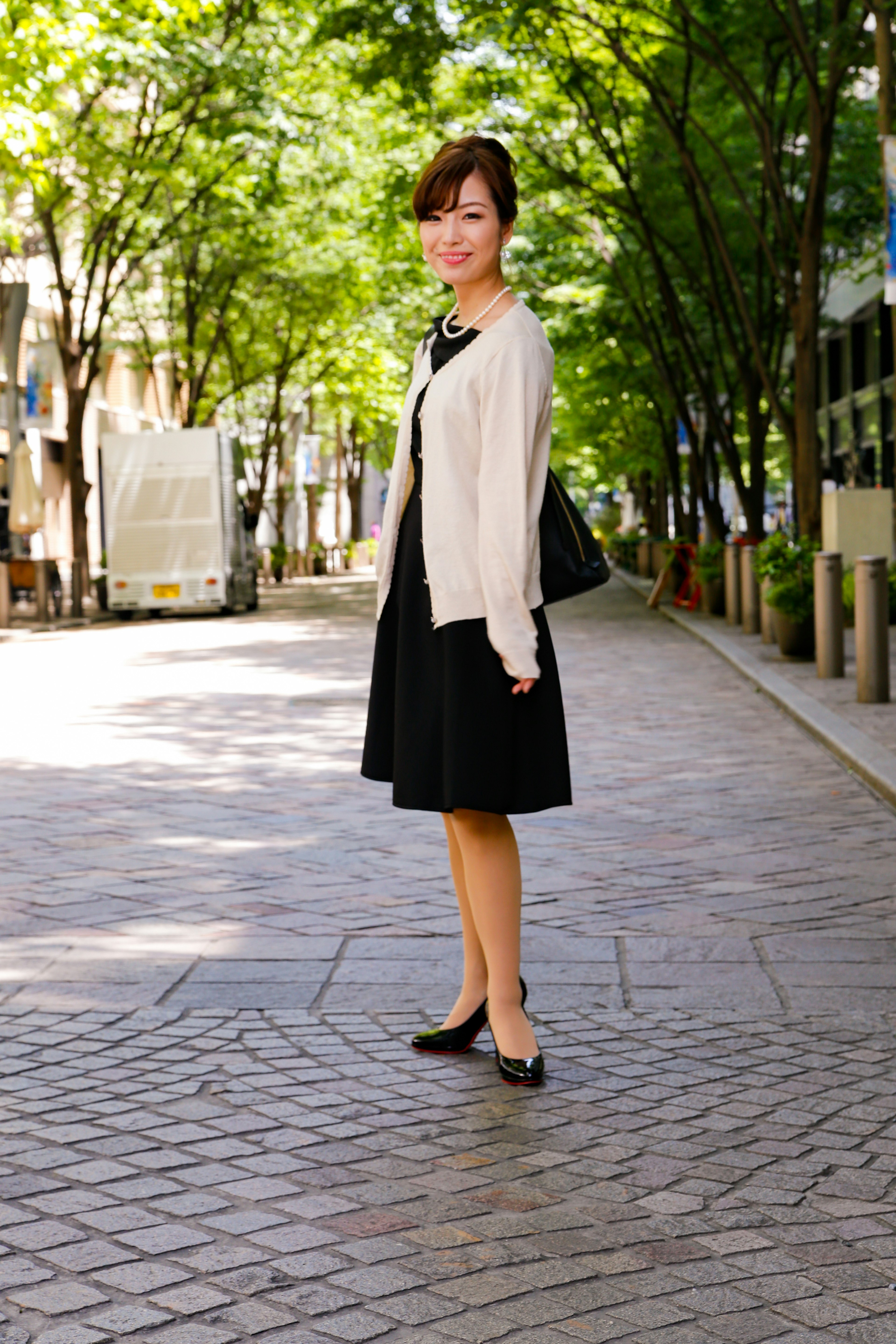 Woman standing in a park wearing a black dress and beige cardigan