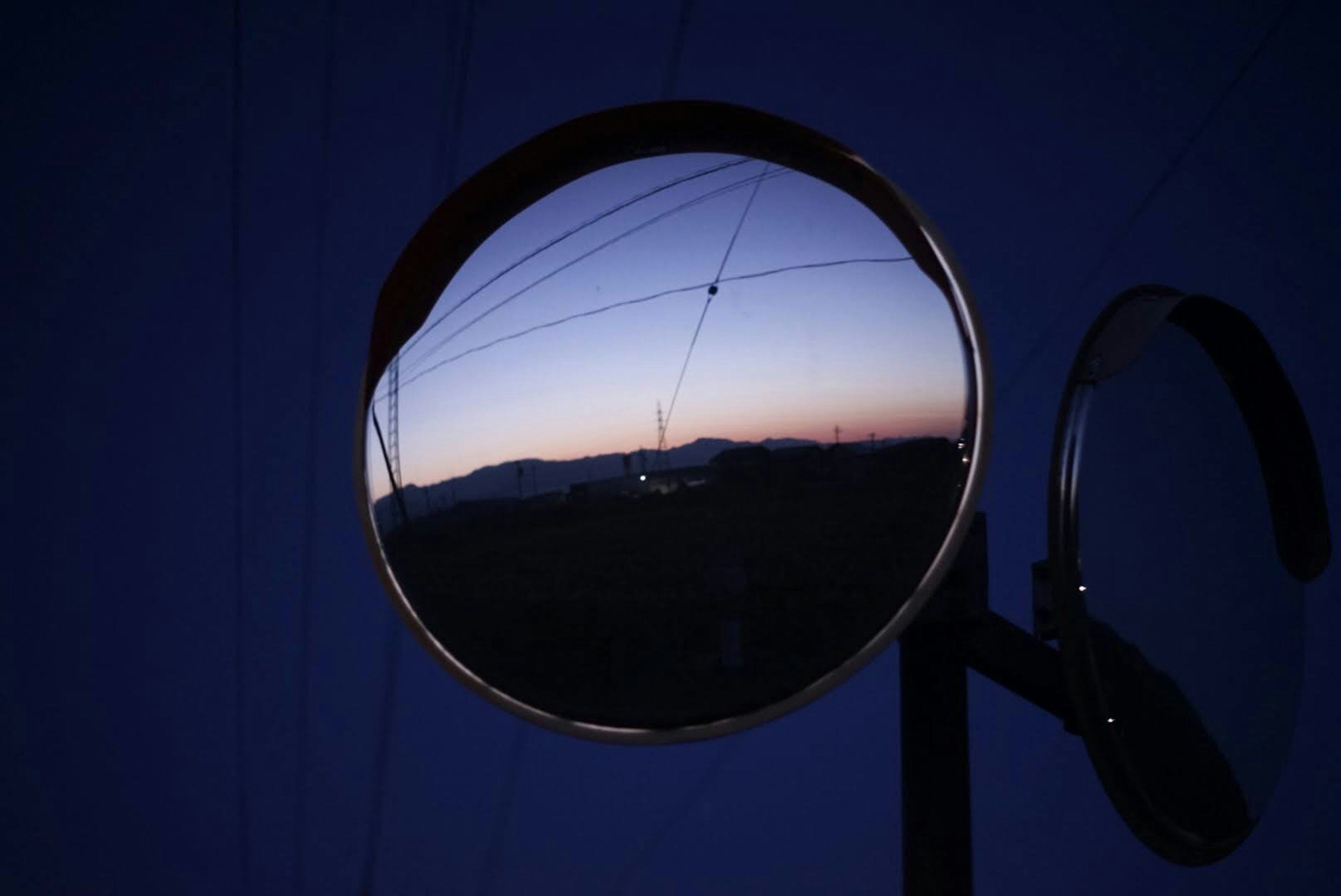 Round mirror reflecting sunset with power lines in the background