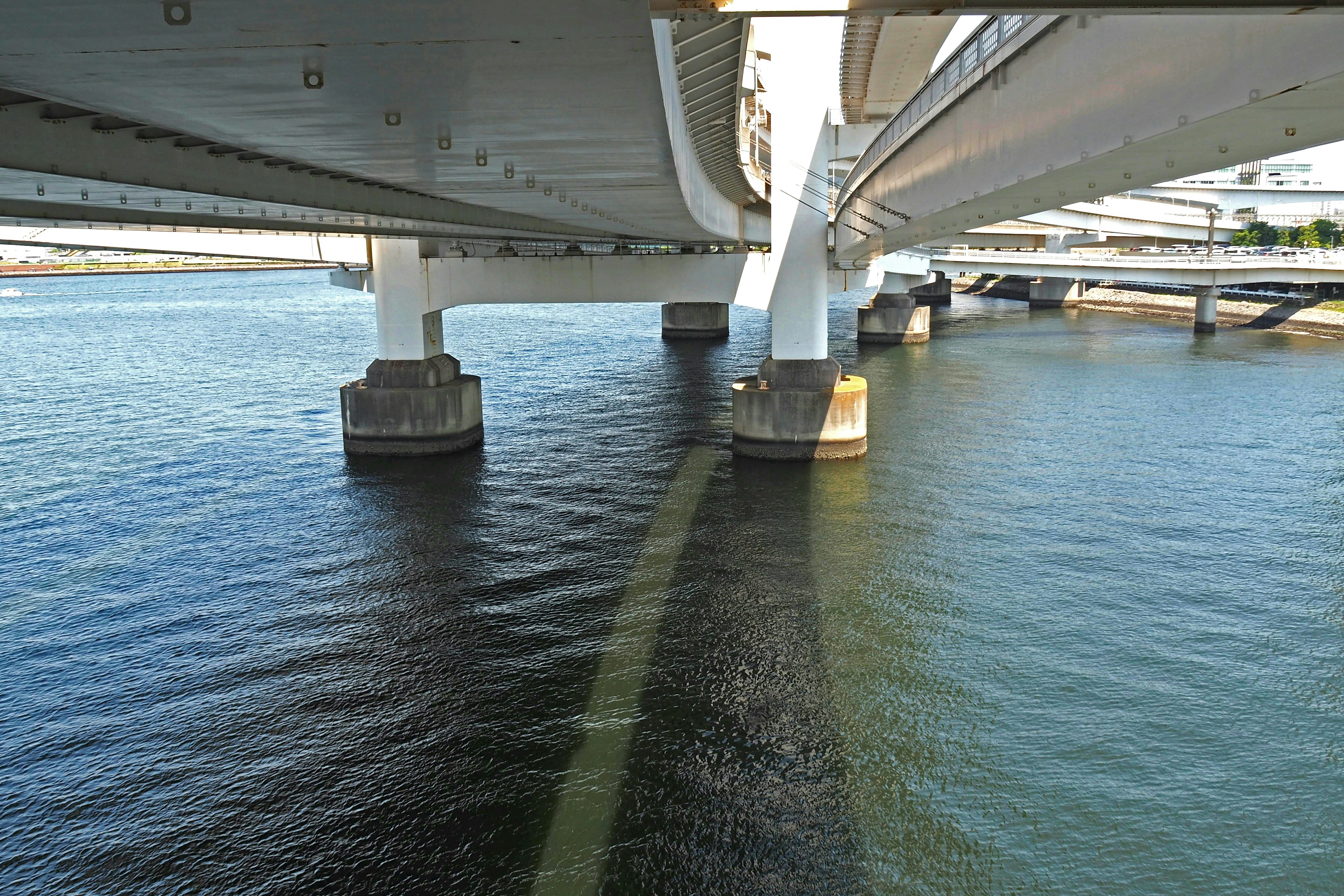 Vue sous un pont montrant des piliers de soutien et des reflets sur l'eau