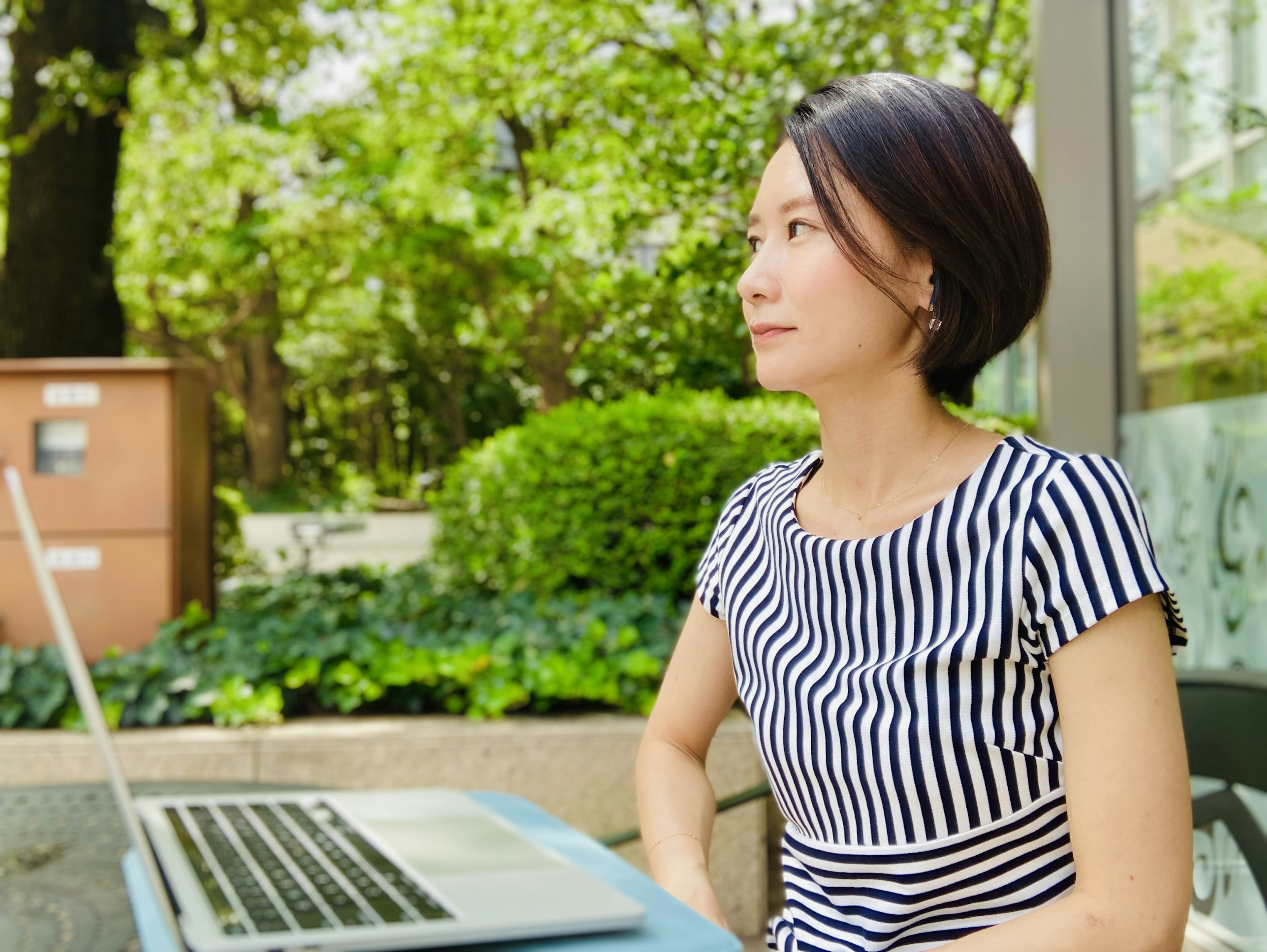 Side profile of a woman using a laptop in a green outdoor setting