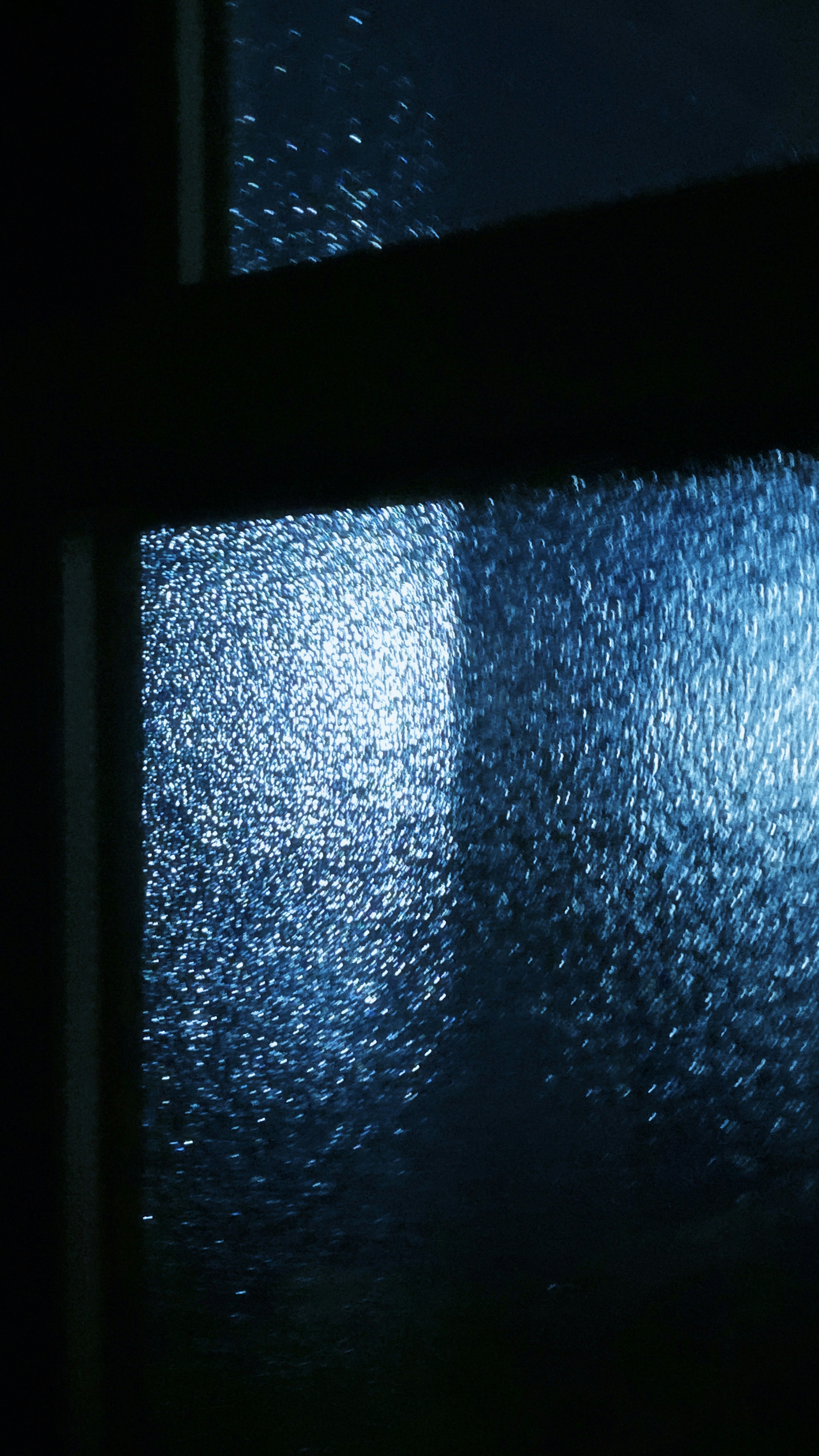 Lumière bleue floue et gouttes d'eau sur une fenêtre en verre la nuit