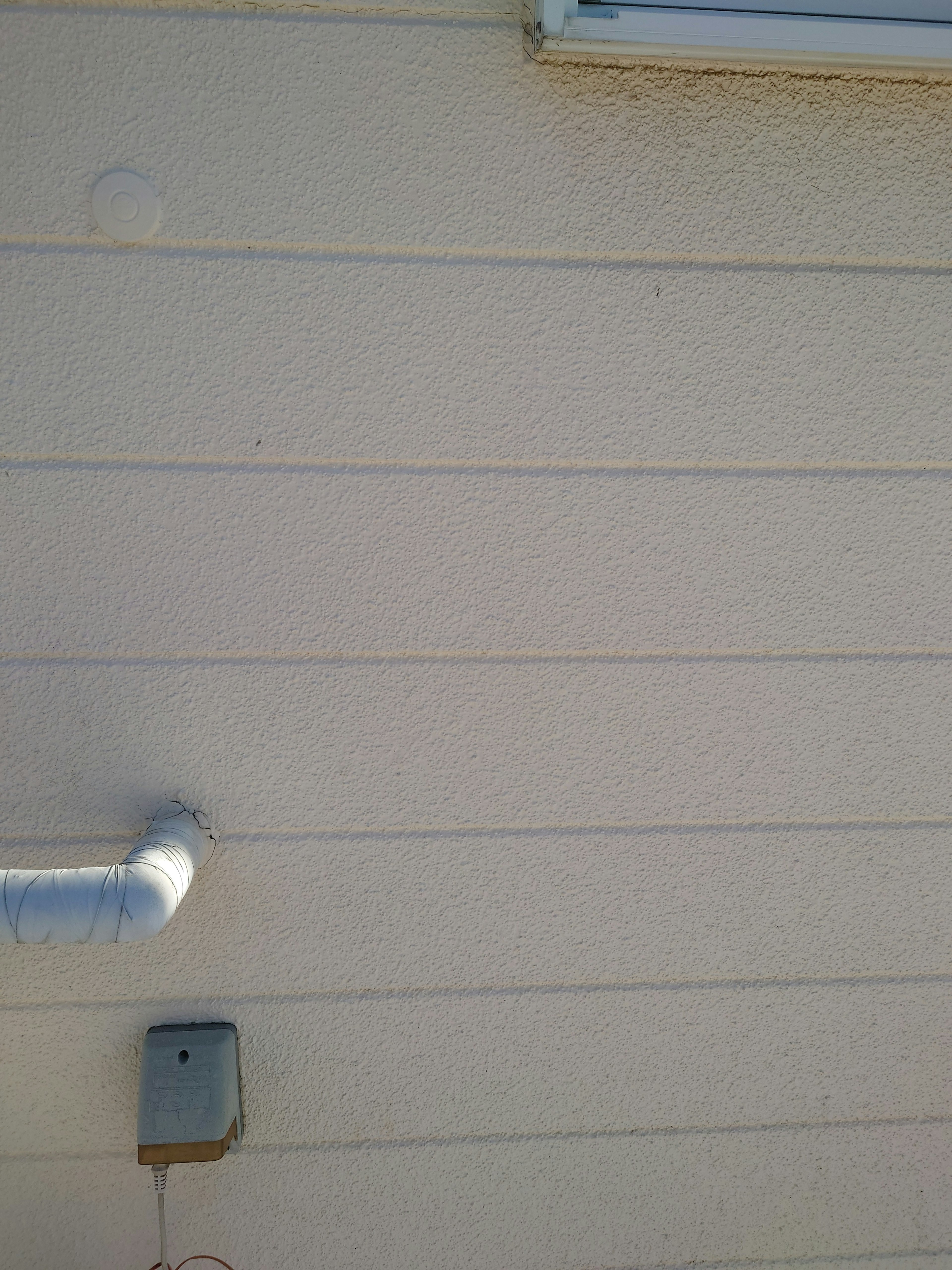 Simple composition of a white exterior wall featuring a metal pipe and an electrical box