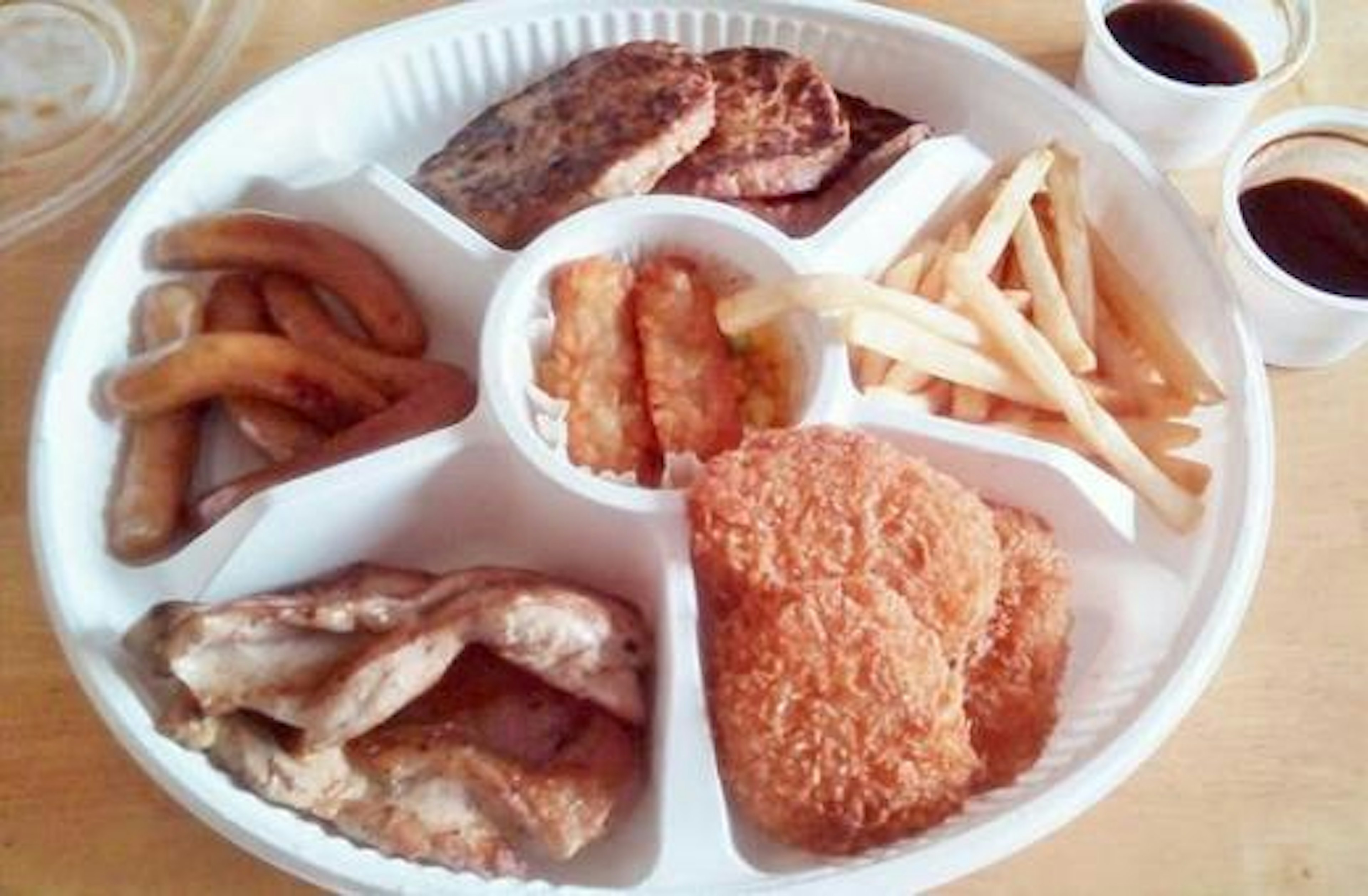 Ein weißer Teller mit verschiedenen Speisen darunter frittiertes Hähnchen gegrilltes Fleisch Pommes Frites und frittierte Bananen