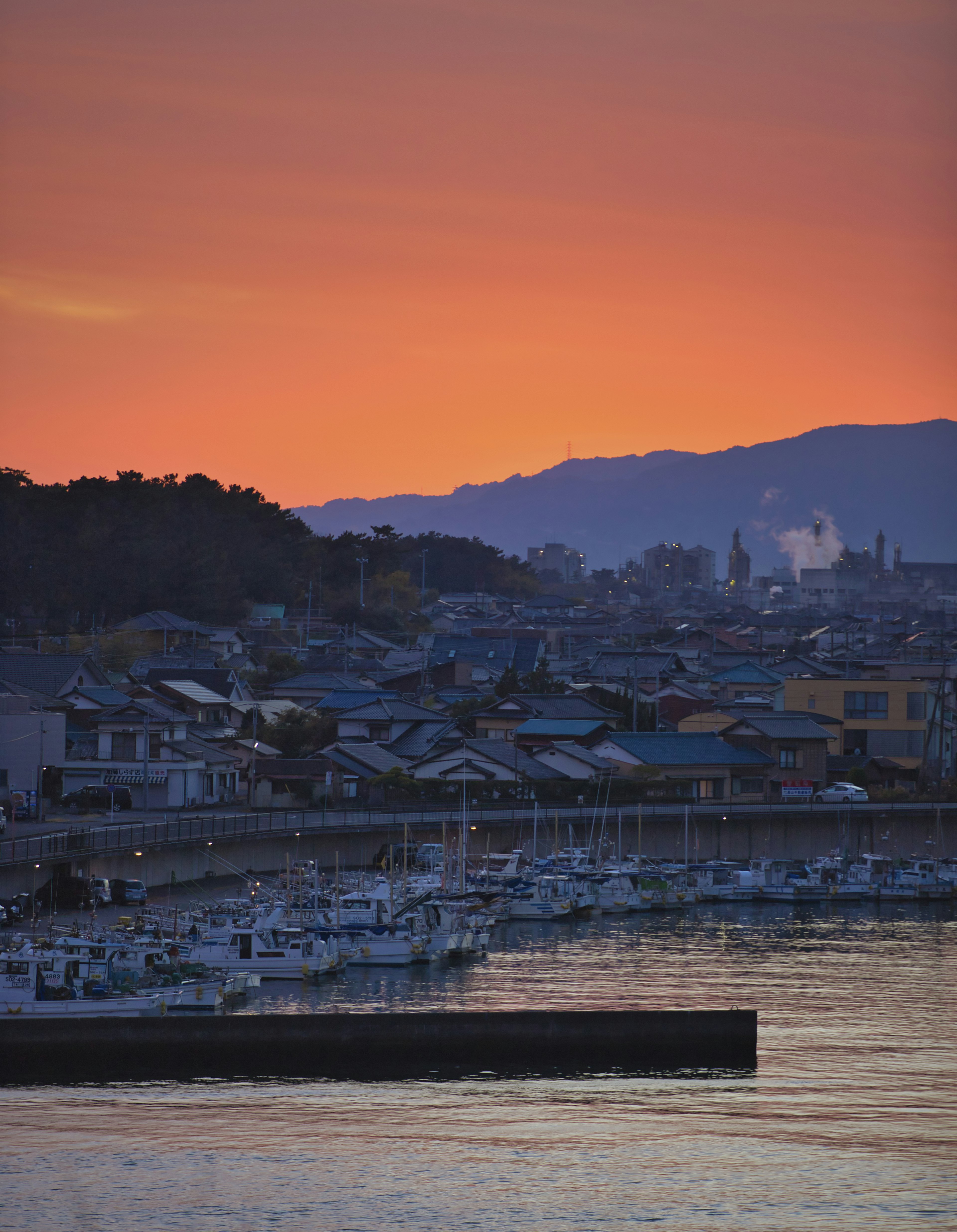 Vista di una città costiera al tramonto con montagne in silhouette e barche ormeggiate