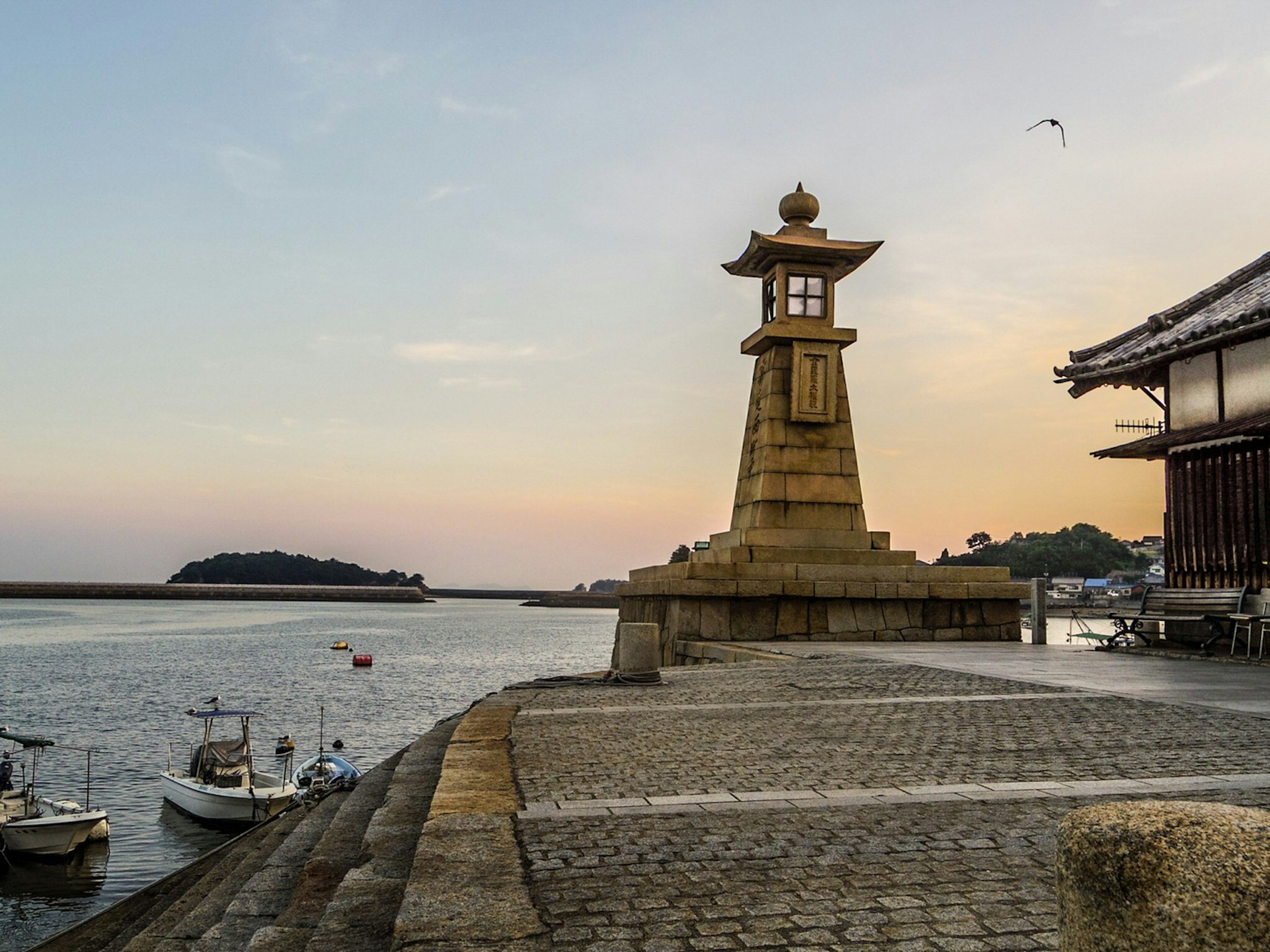 Coastal scene at sunset featuring a lighthouse and fishing boats