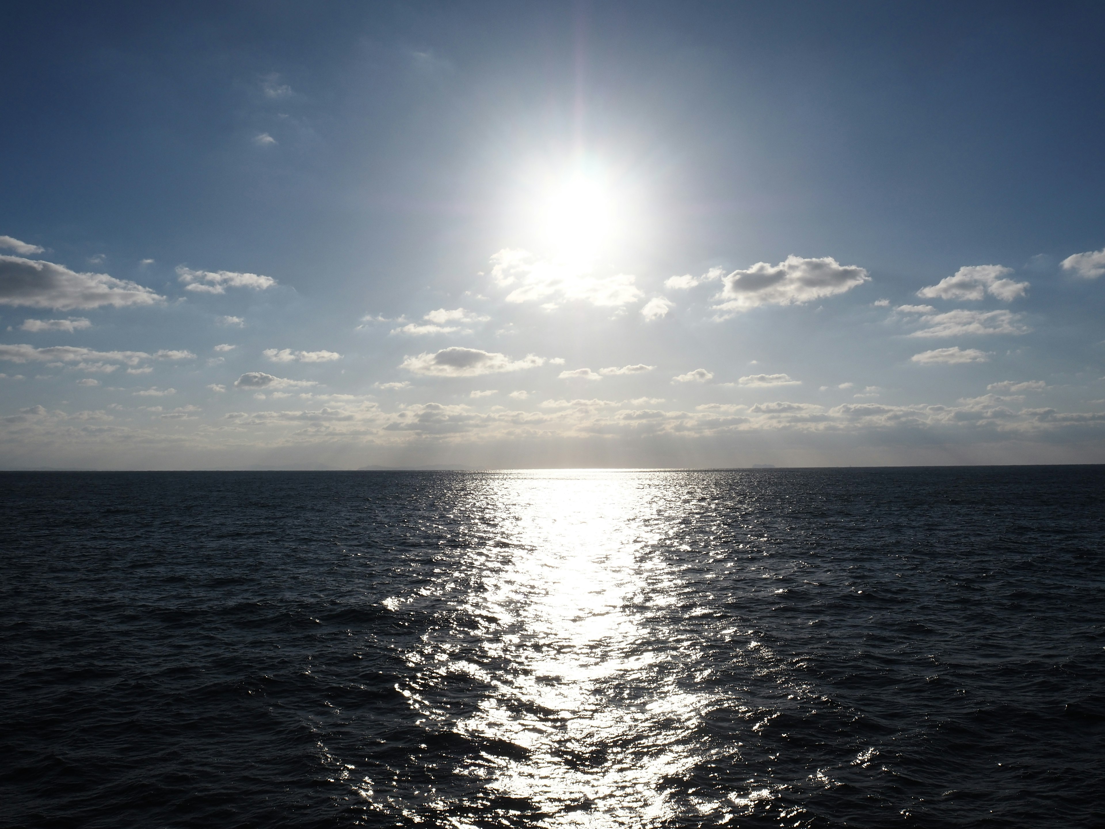 Bright sun over the shimmering ocean with scattered clouds