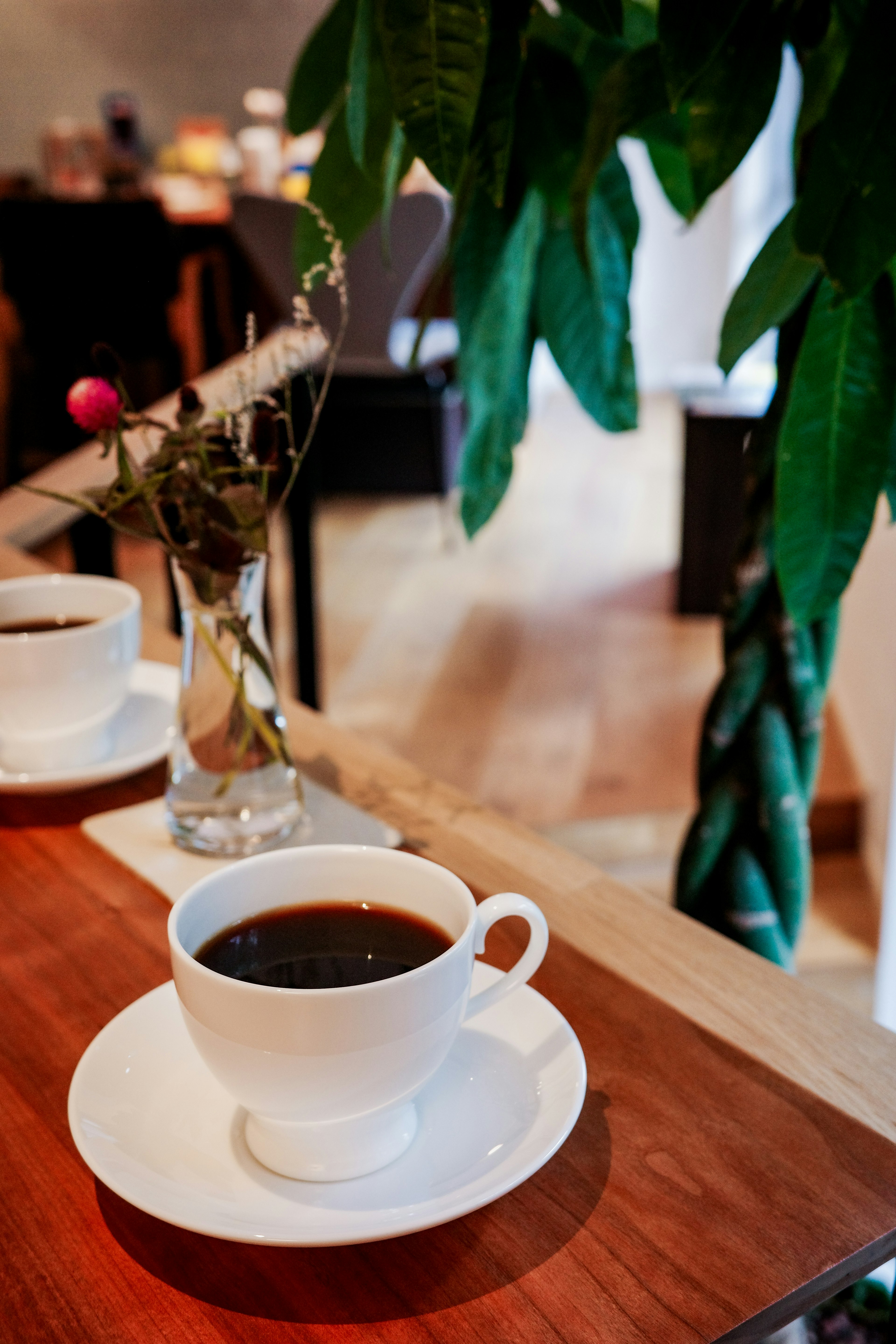 カフェのテーブルに置かれた白いカップのコーヒーと花瓶の花