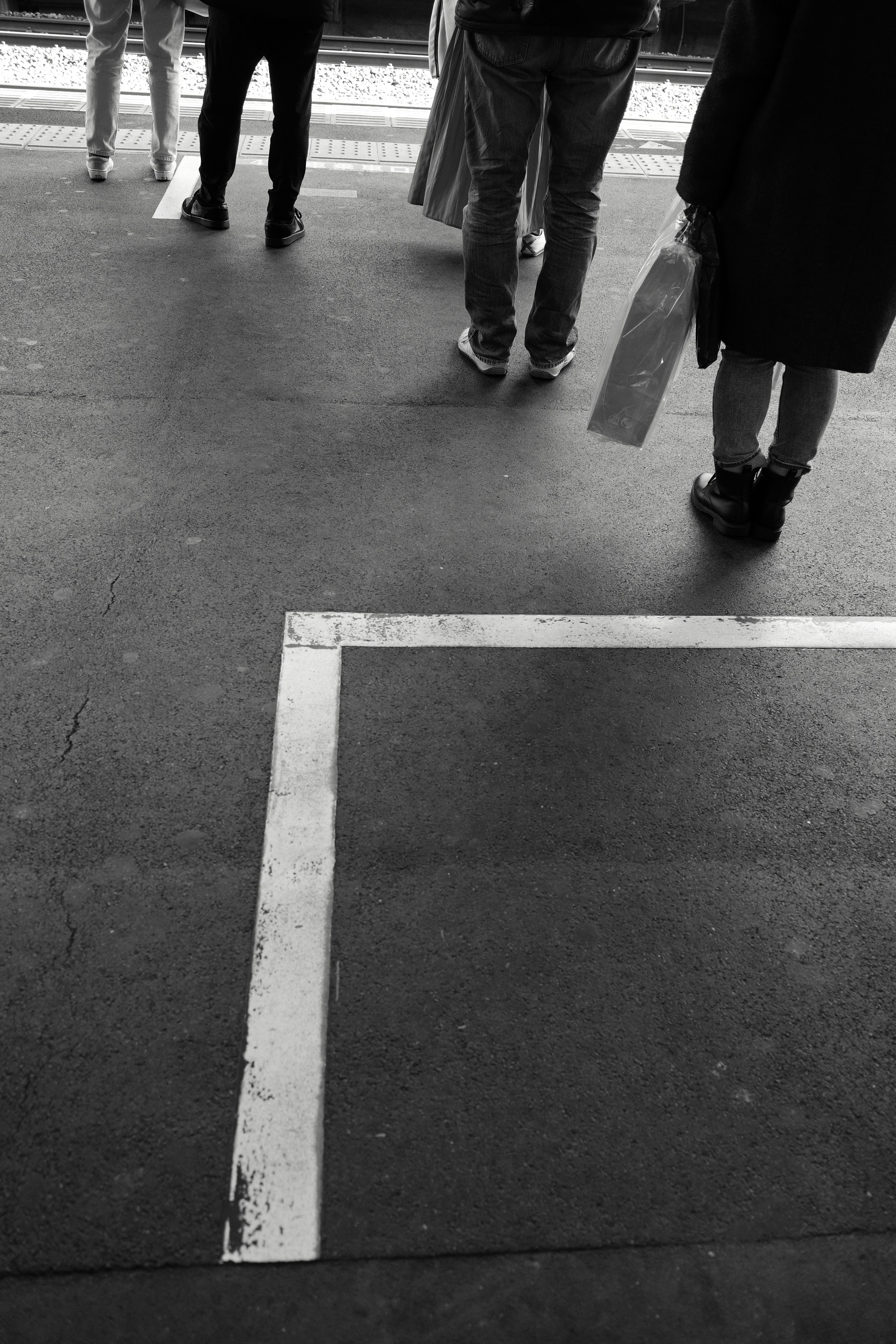 Black and white photo of people's feet standing on a train platform