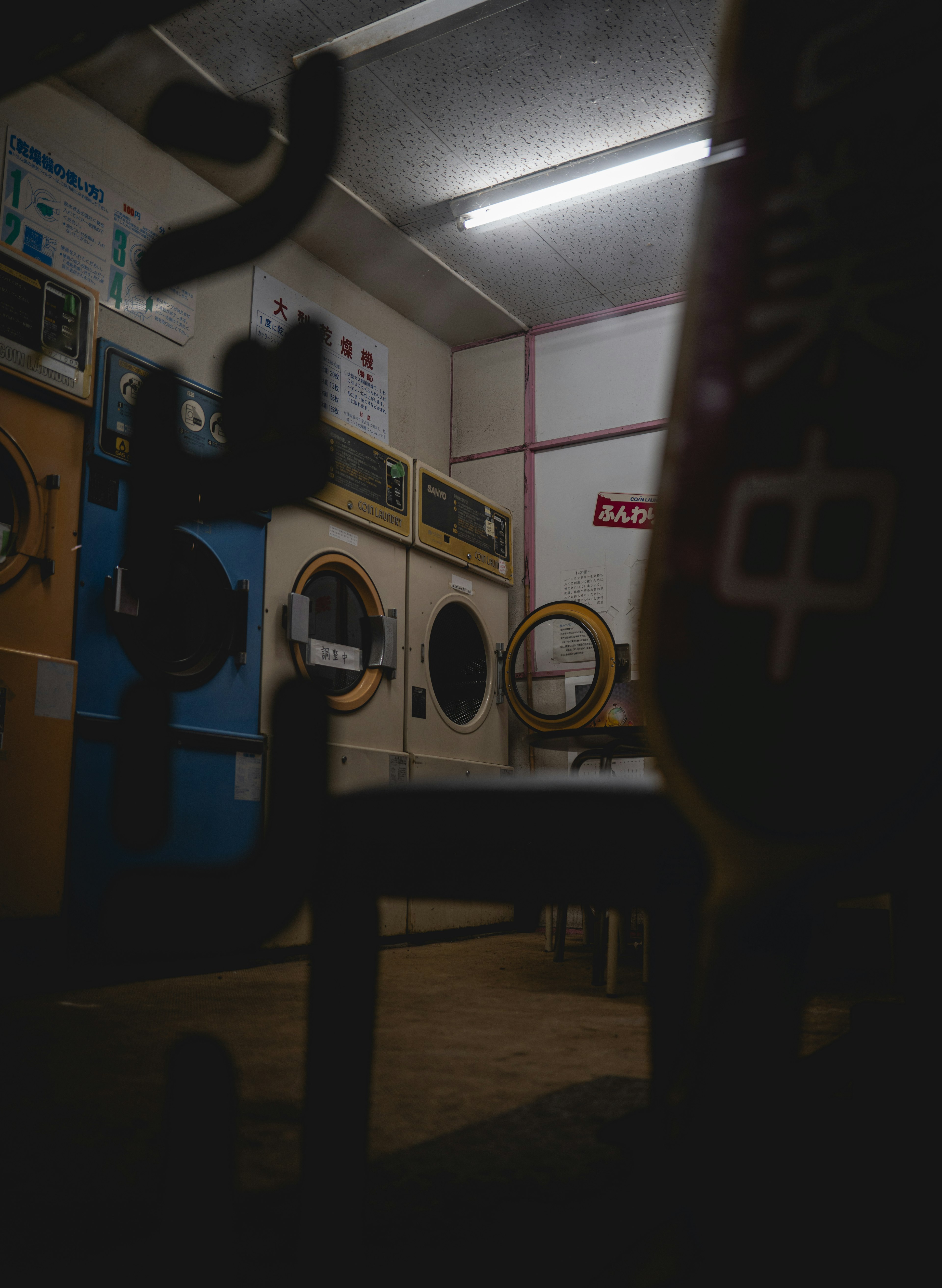 Interior of a dimly lit laundry room featuring washing machines and a chair