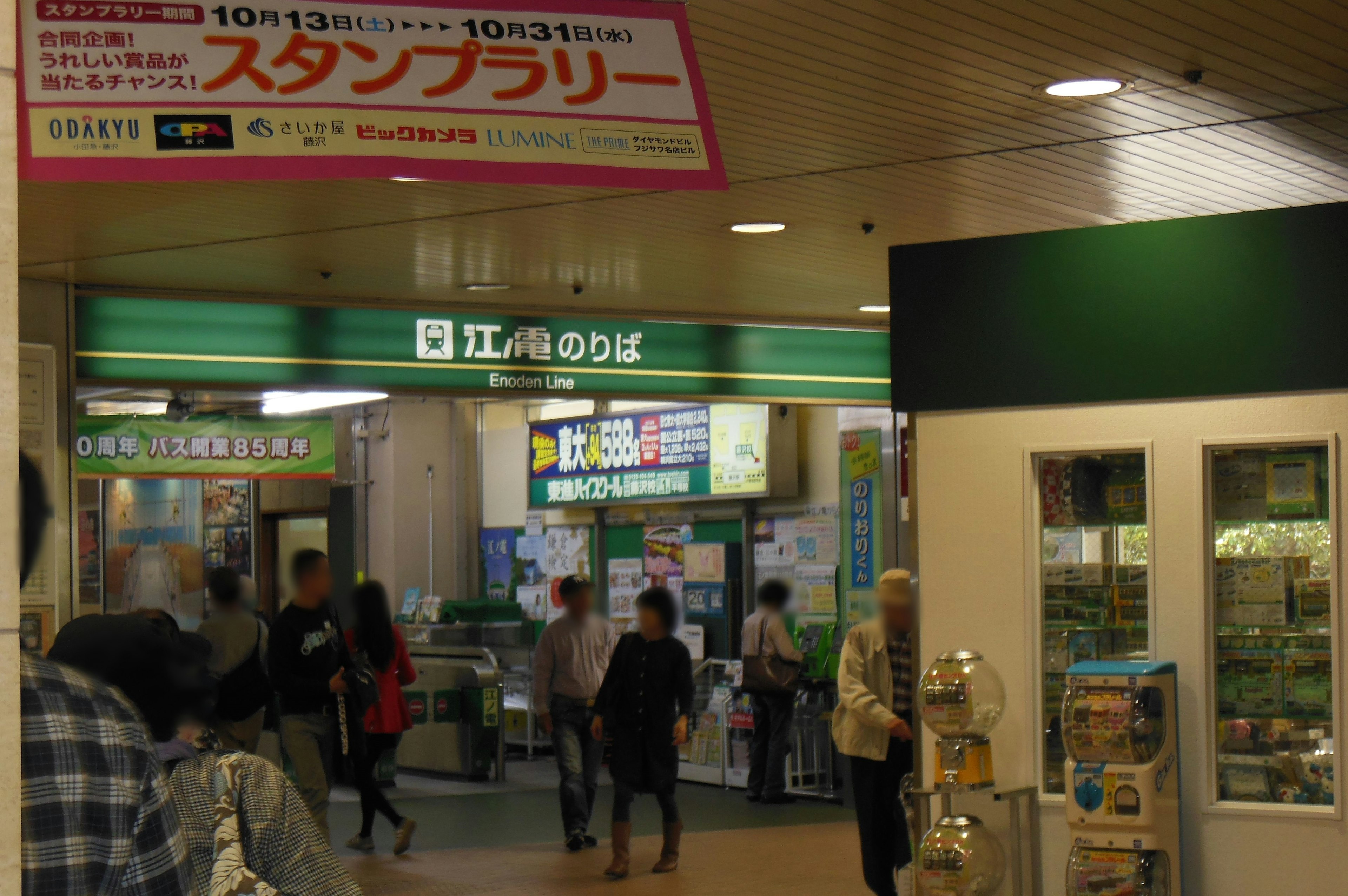 駅の入り口にある緑の看板と人々の行き交う様子