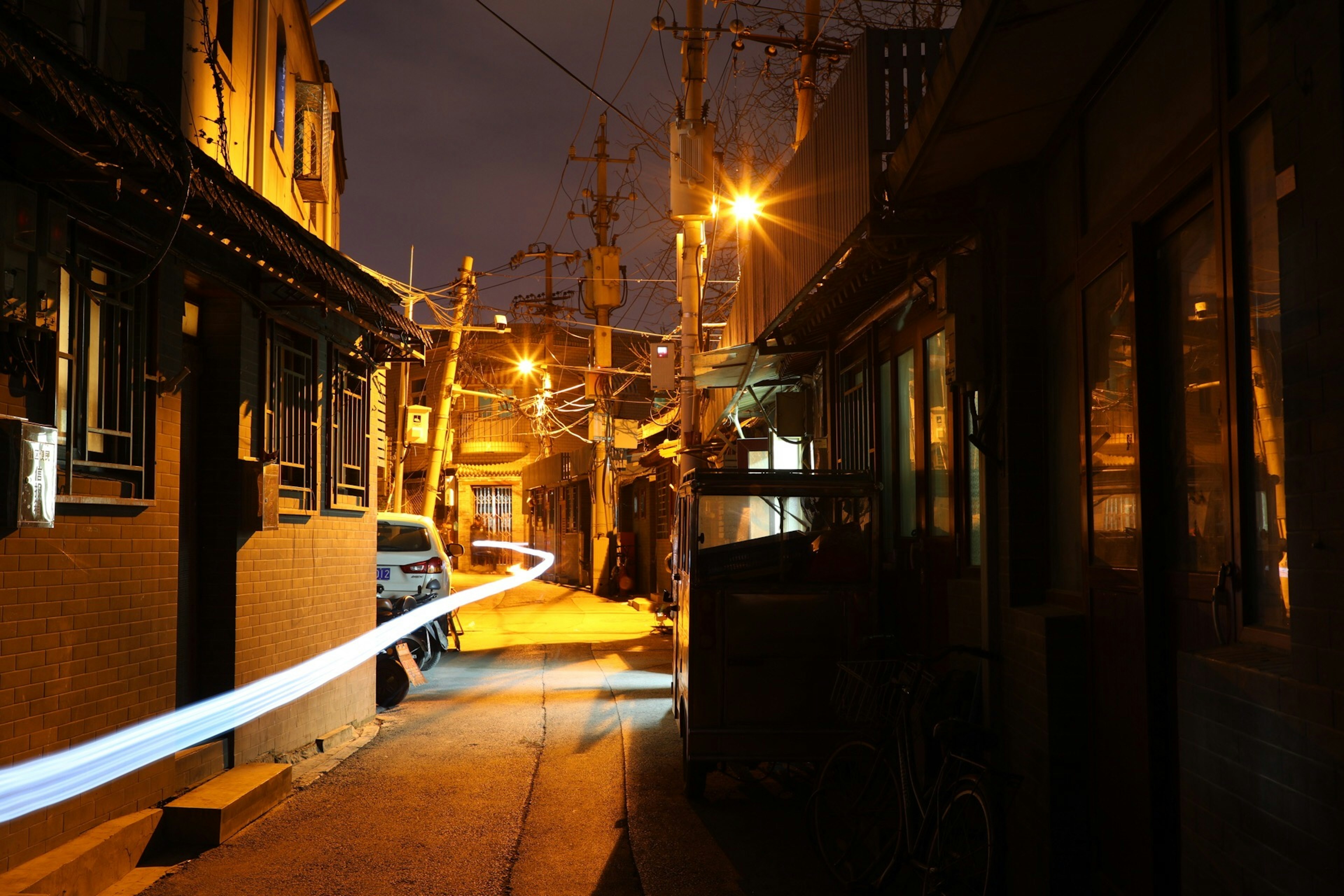 Allée étroite la nuit éclairée par des lampadaires orange chaud avec une traînée de lumière bleue