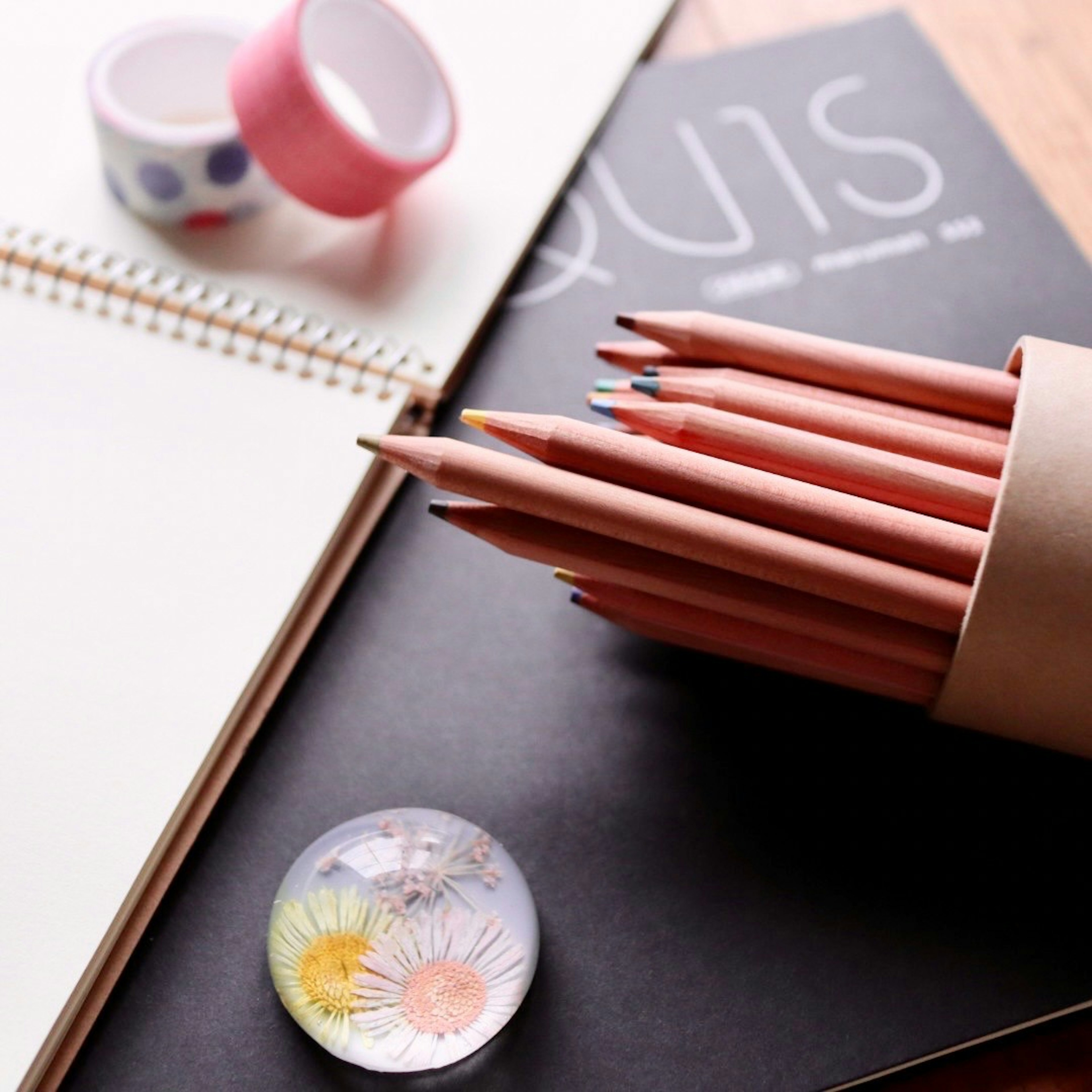 Lápices de colores dispuestos junto a un cuaderno de bocetos y cinta decorativa