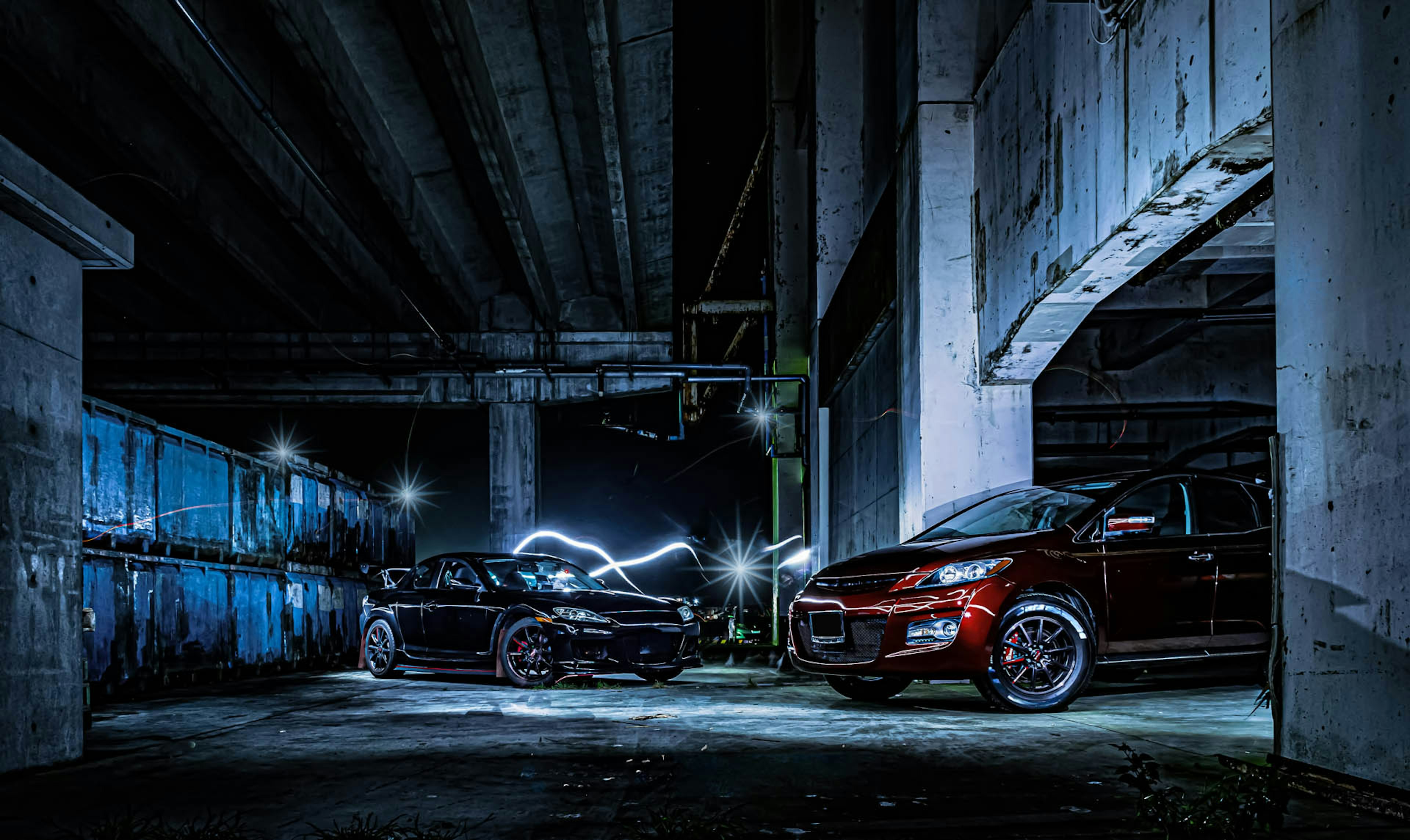 Dos coches estacionados en un área oscura con un fondo industrial