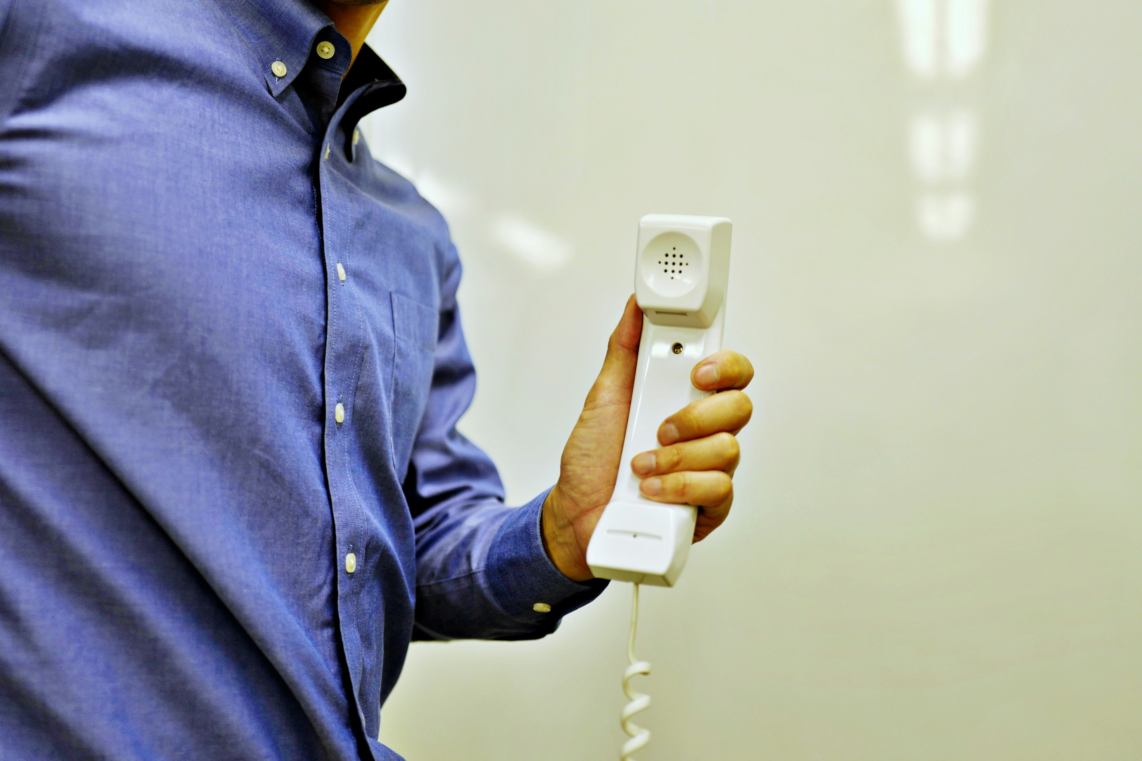 Homme en chemise bleue tenant un combiné téléphonique blanc