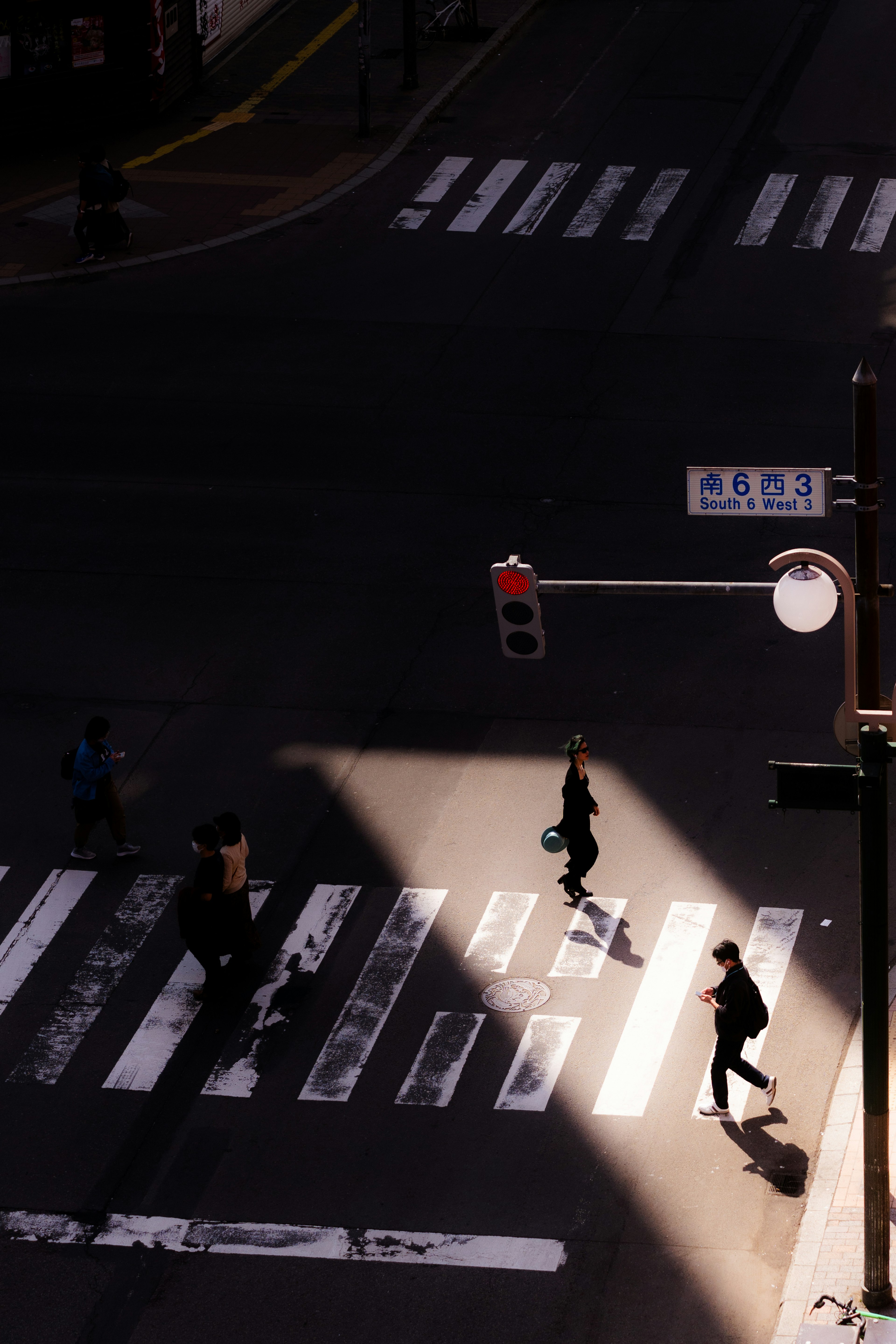 People crossing a street at a crosswalk with shadows and a red traffic light