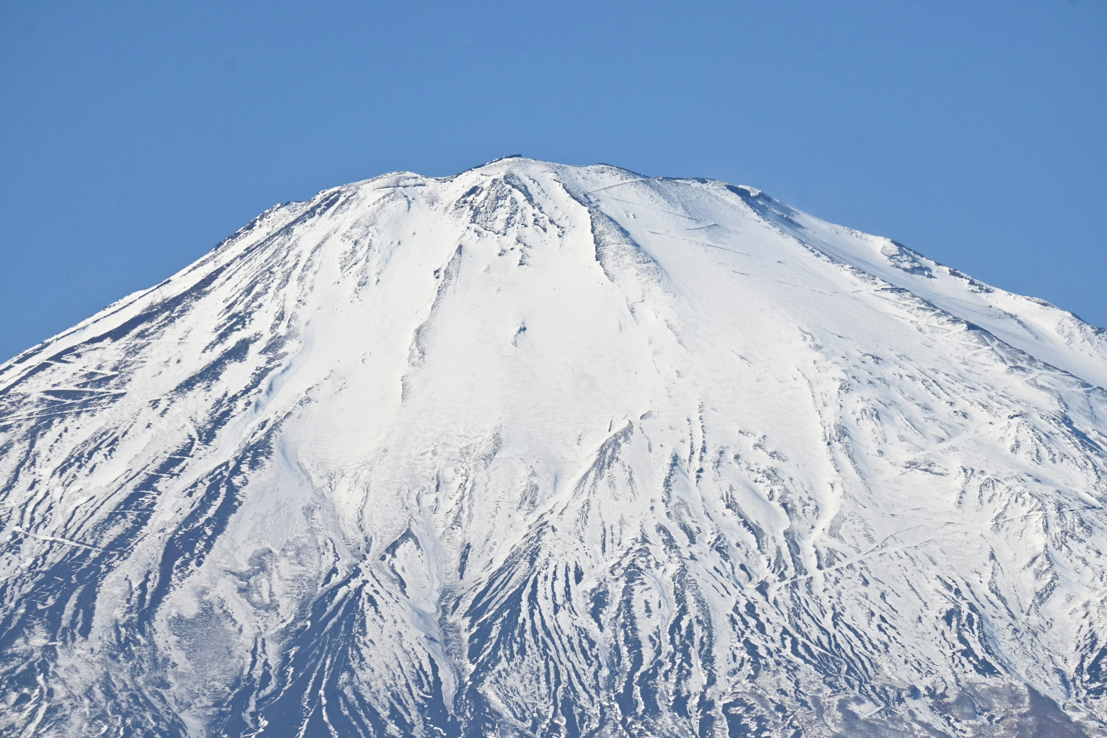 Snow-covered peak of Mount Fuji against a clear blue sky