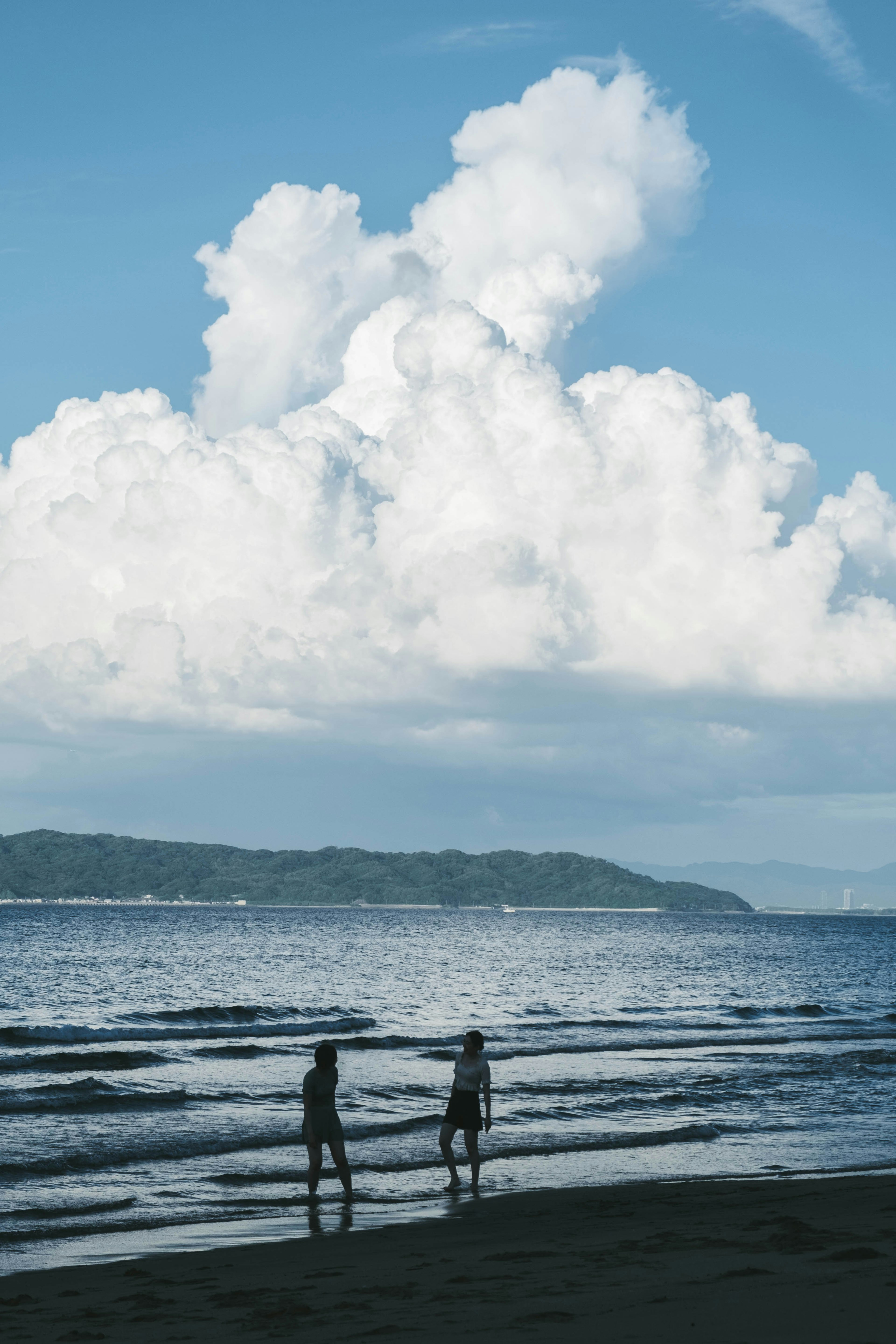 海岸で立つ二人のシルエットと青い空の大きな雲