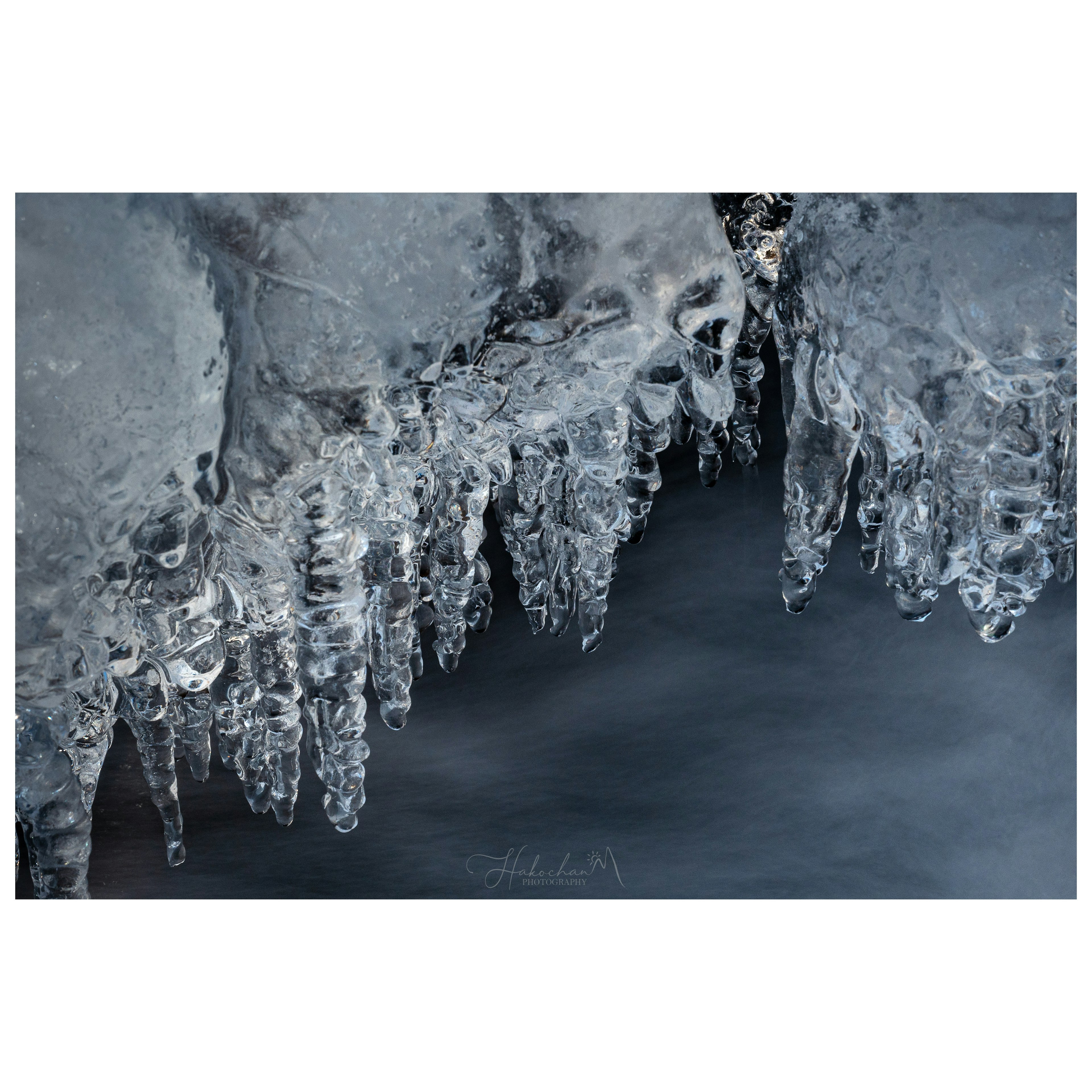 Eiszapfen hängen von einer gefrorenen Oberfläche mit einem dunklen Wasserhintergrund