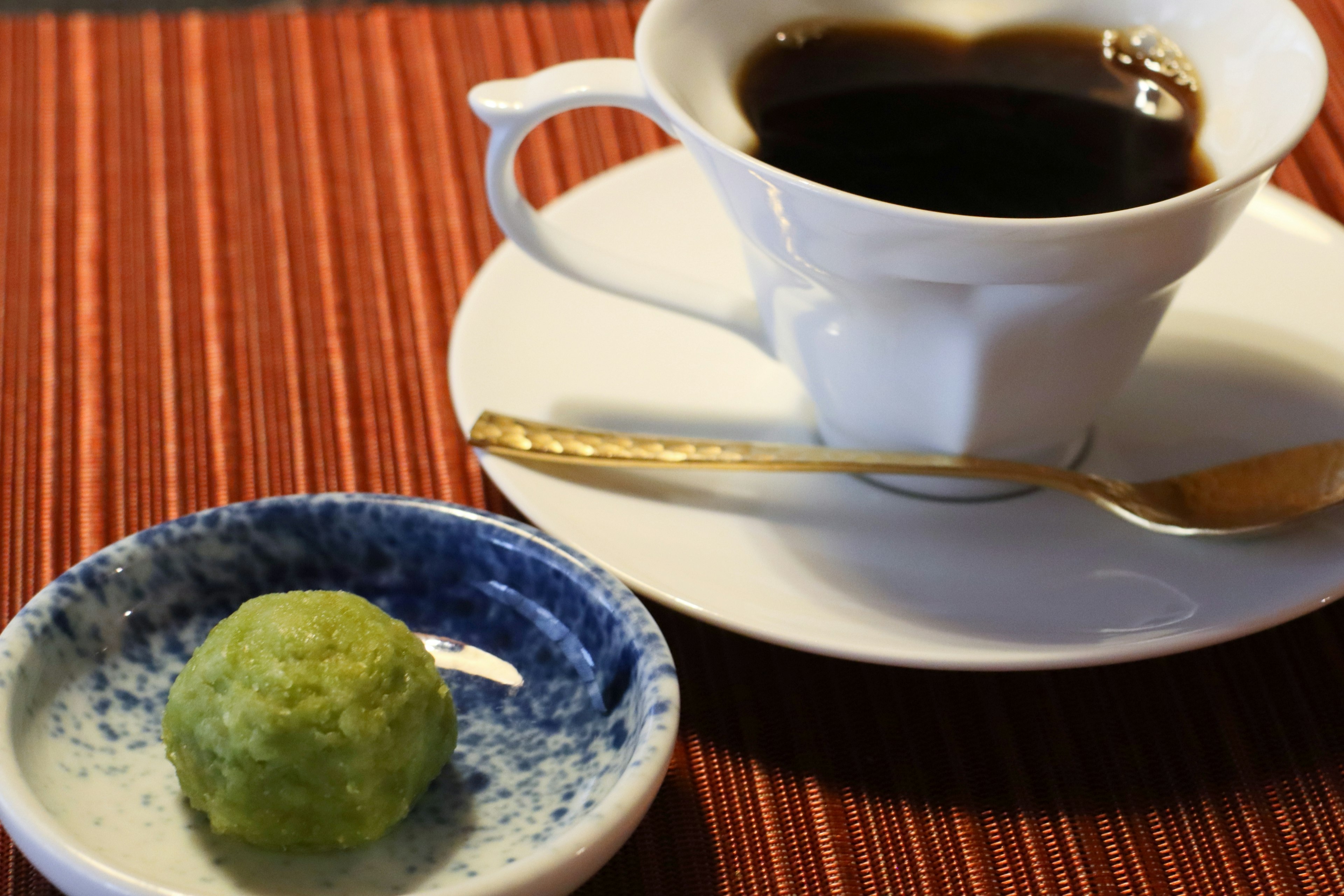 Kaffee in einer weißen Tasse mit einer grünen Süßigkeit auf einem blauen Teller