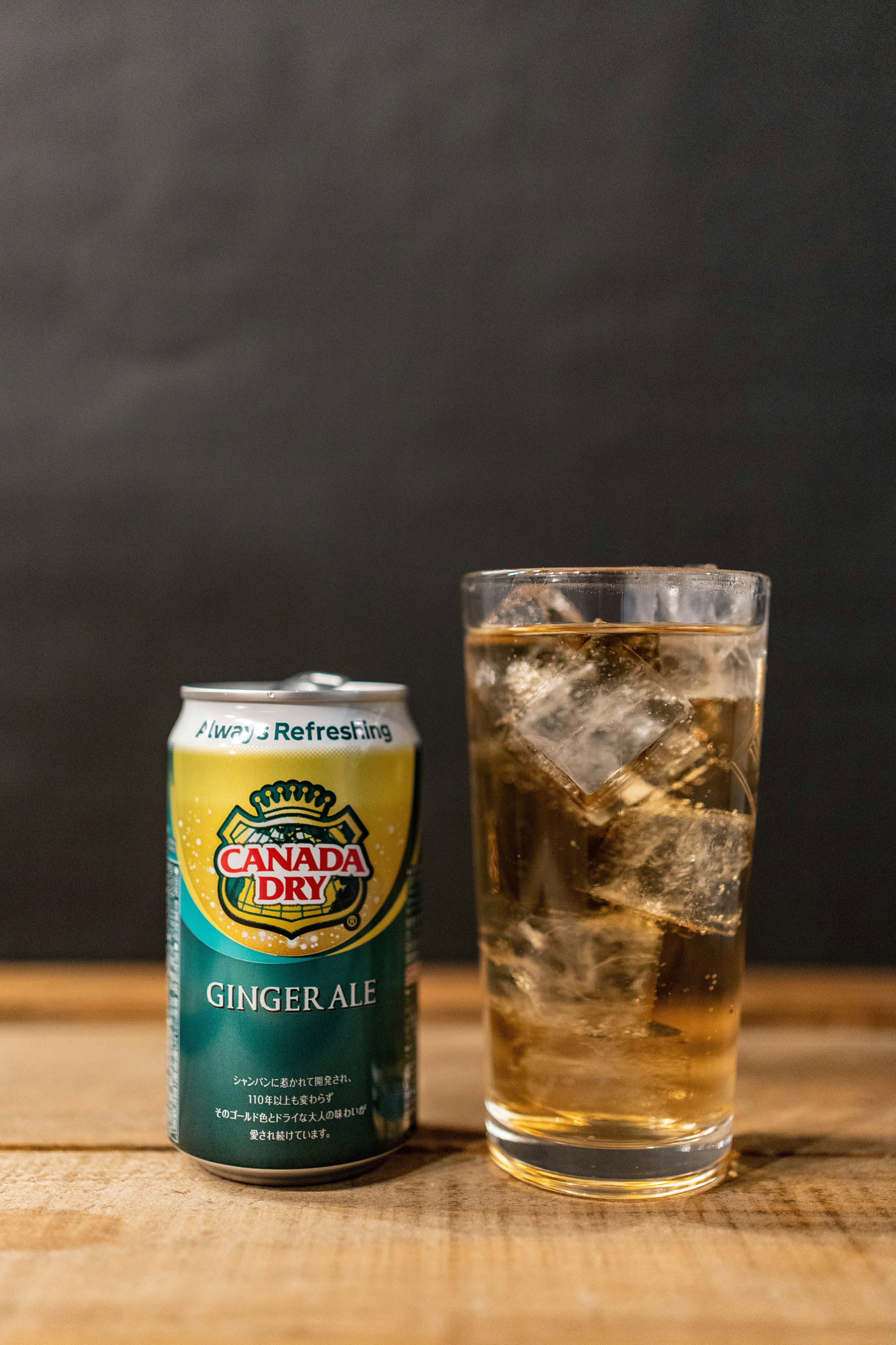 Una lata de ginger ale junto a un vaso lleno de hielo y ginger ale sobre una mesa de madera