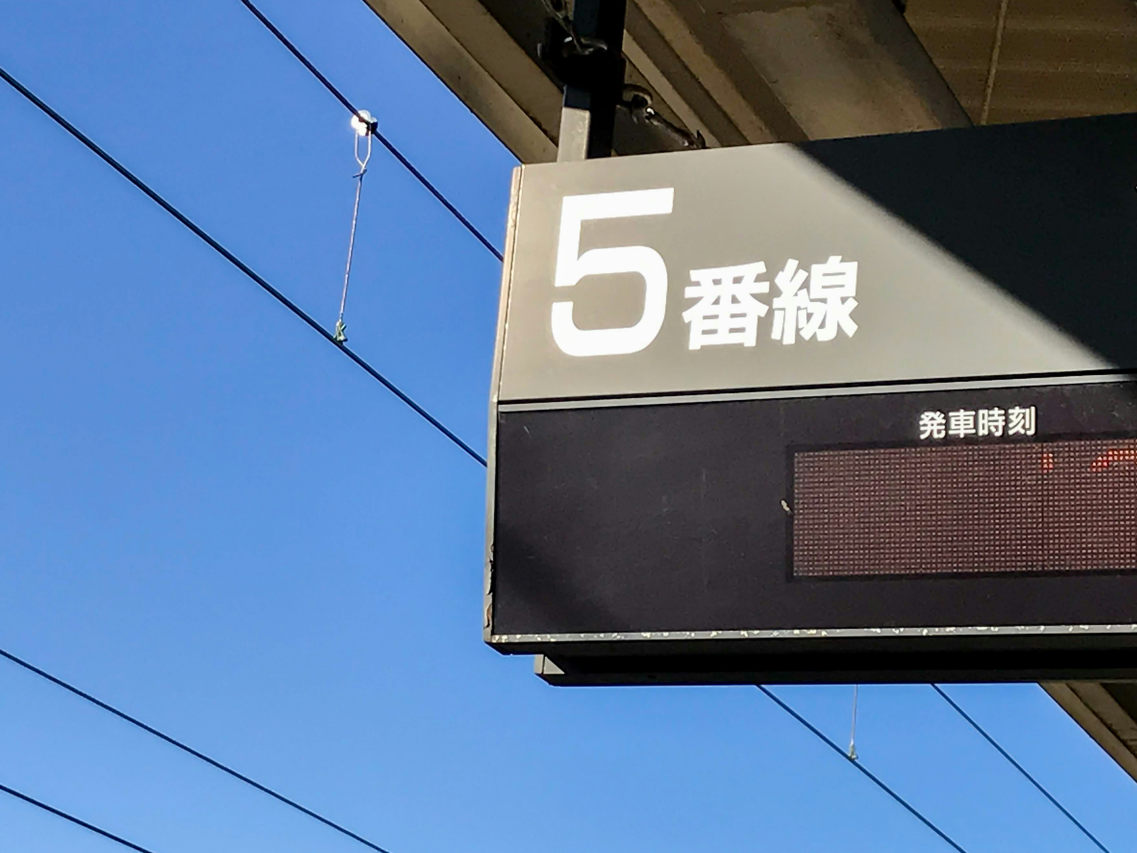 Papan stasiun untuk jalur nomor 5 di bawah langit biru yang cerah