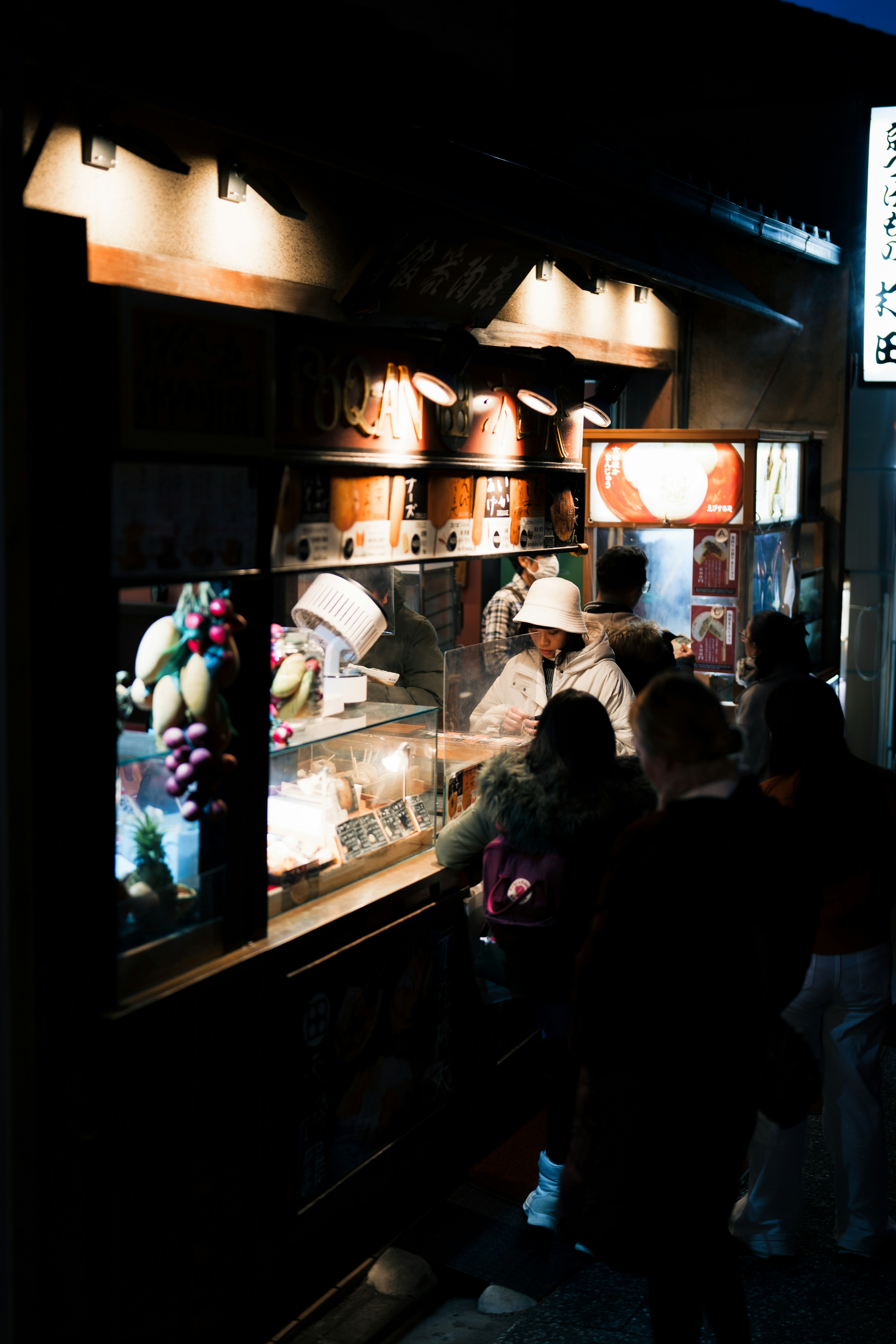 Puesto de mercado nocturno vendiendo frutas con clientes y vendedor