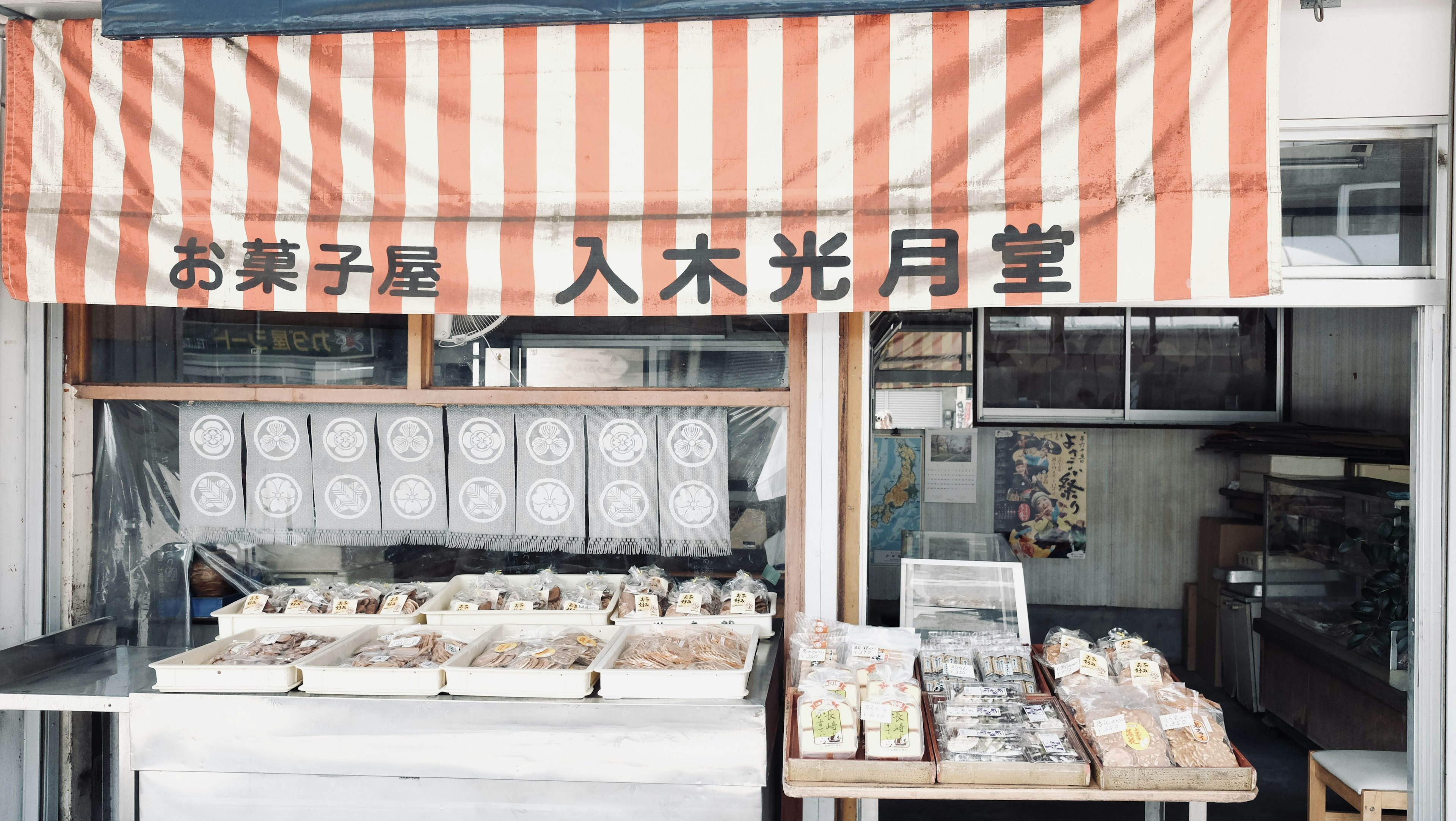 Exterior de una tienda de dulces japoneses tradicionales con toldo a rayas rojas y blancas y productos exhibidos