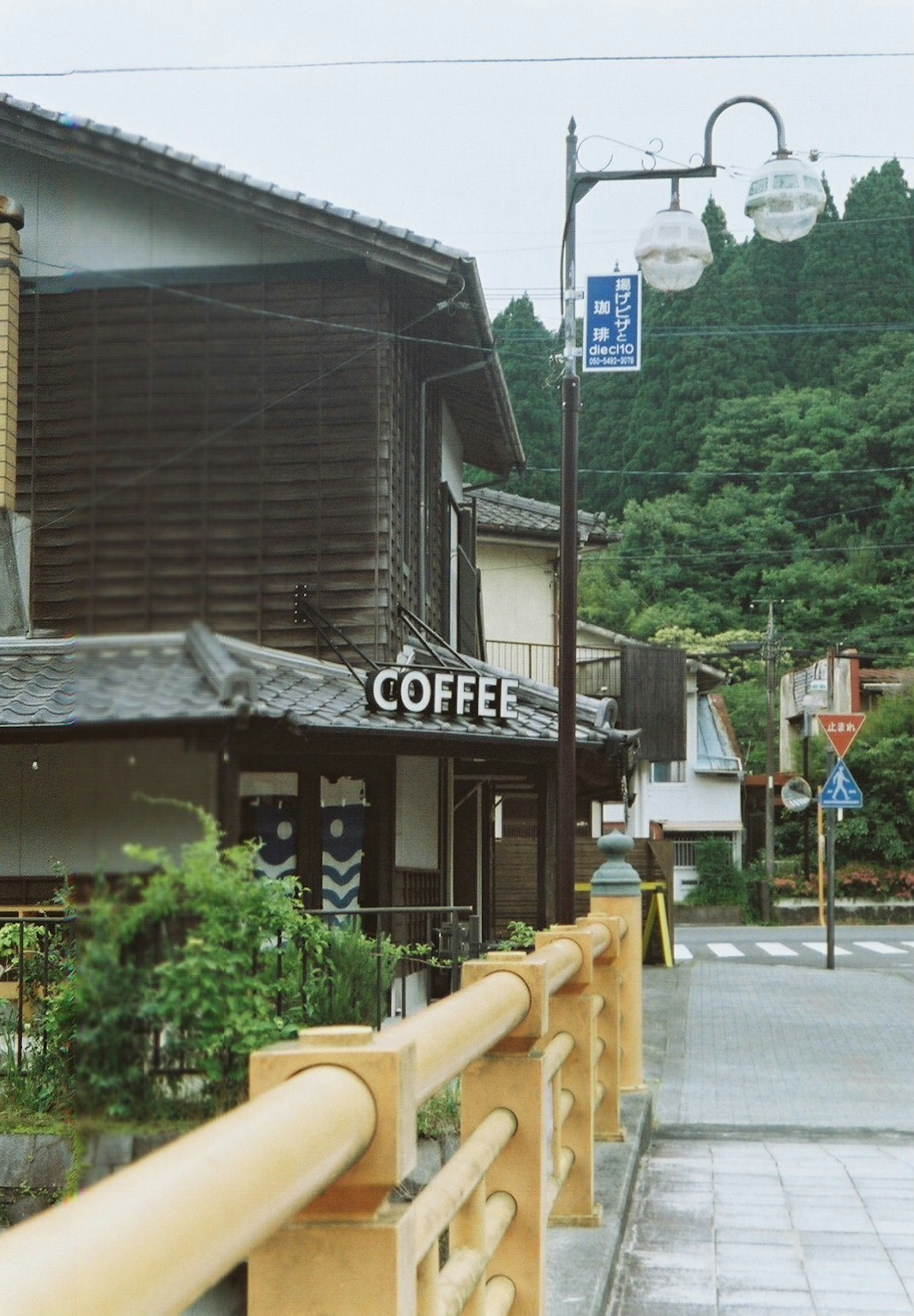 ด้านนอกของร้านกาแฟในเมืองญี่ปุ่นแบบดั้งเดิมพร้อมสถาปัตยกรรมไม้และพื้นหลังสีเขียว