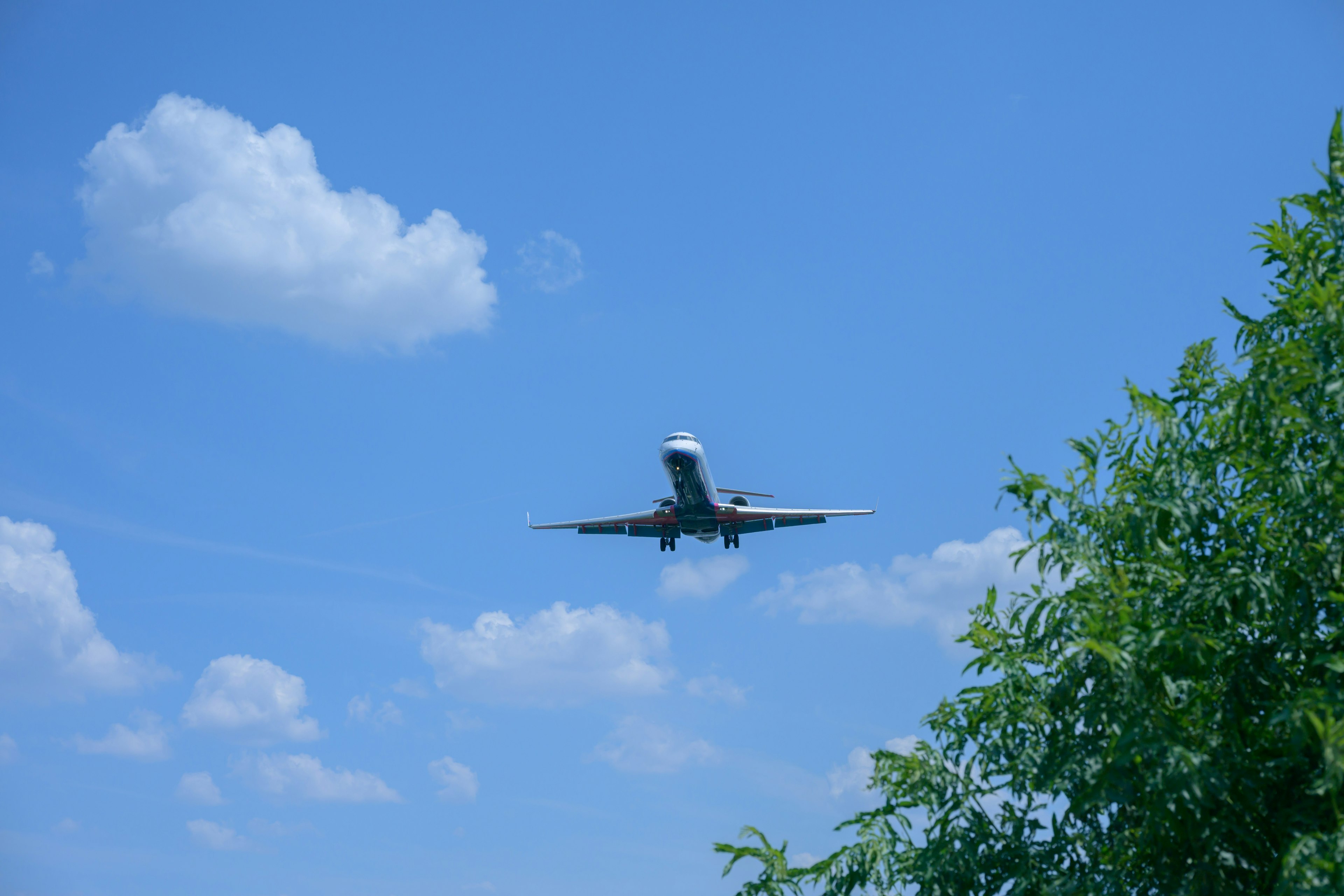 Un aereo che vola in un cielo blu con nuvole e alberi verdi