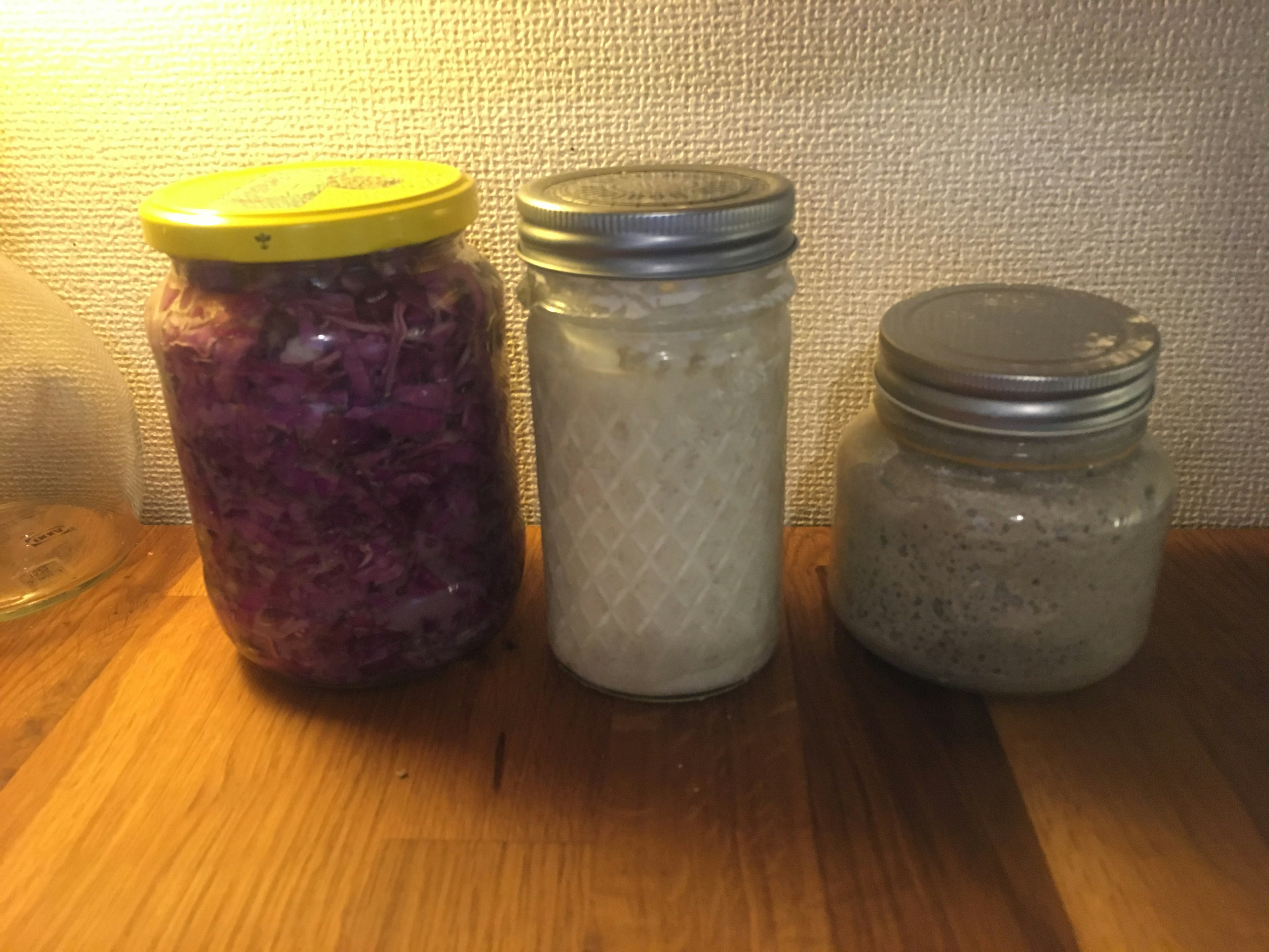 Tres frascos de alimentos fermentados que incluyen repollo morado, fermentación blanca y fermentación gris en una encimera de madera