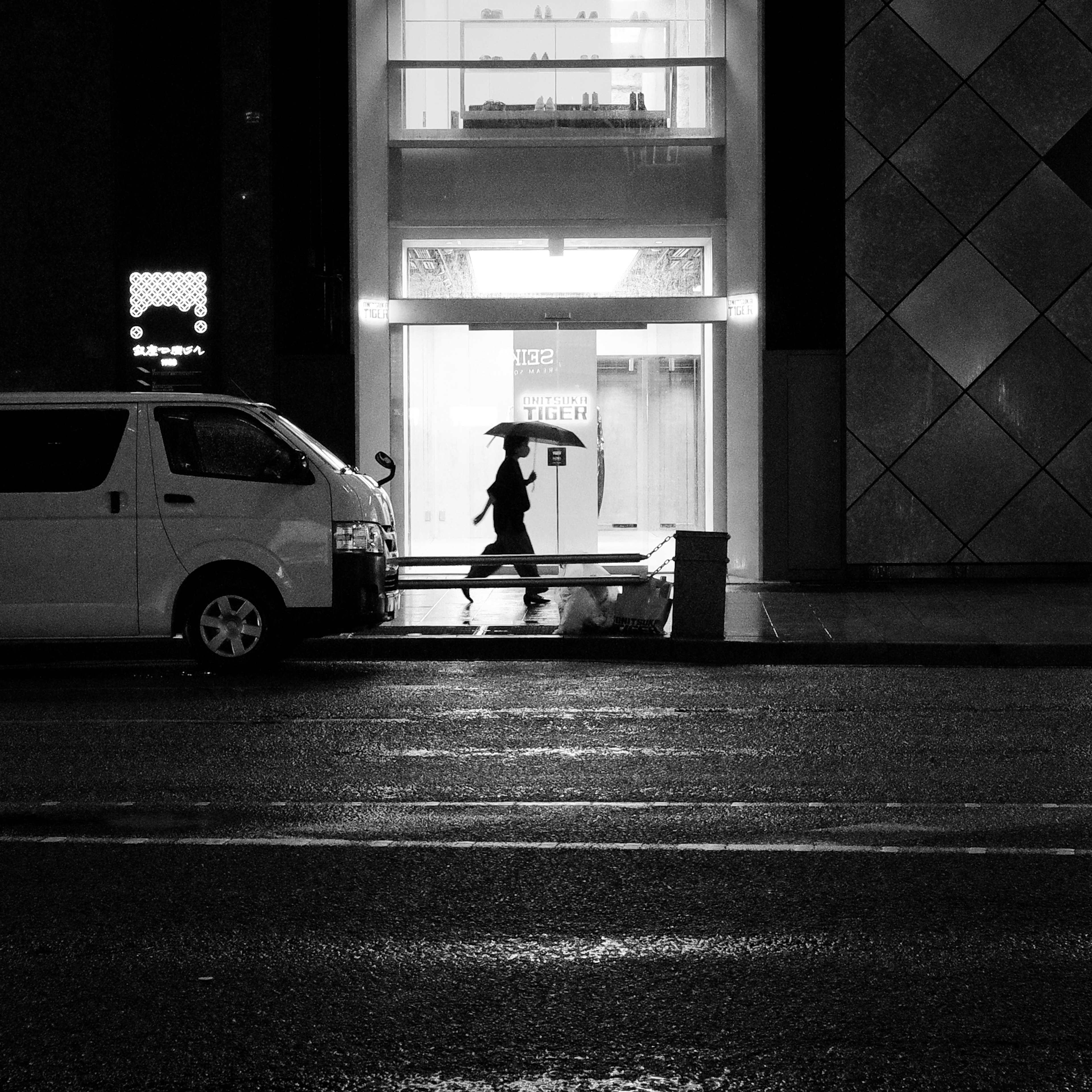 Schwarzweißfoto einer Person, die mit einem Regenschirm an einem regnerischen Abend geht