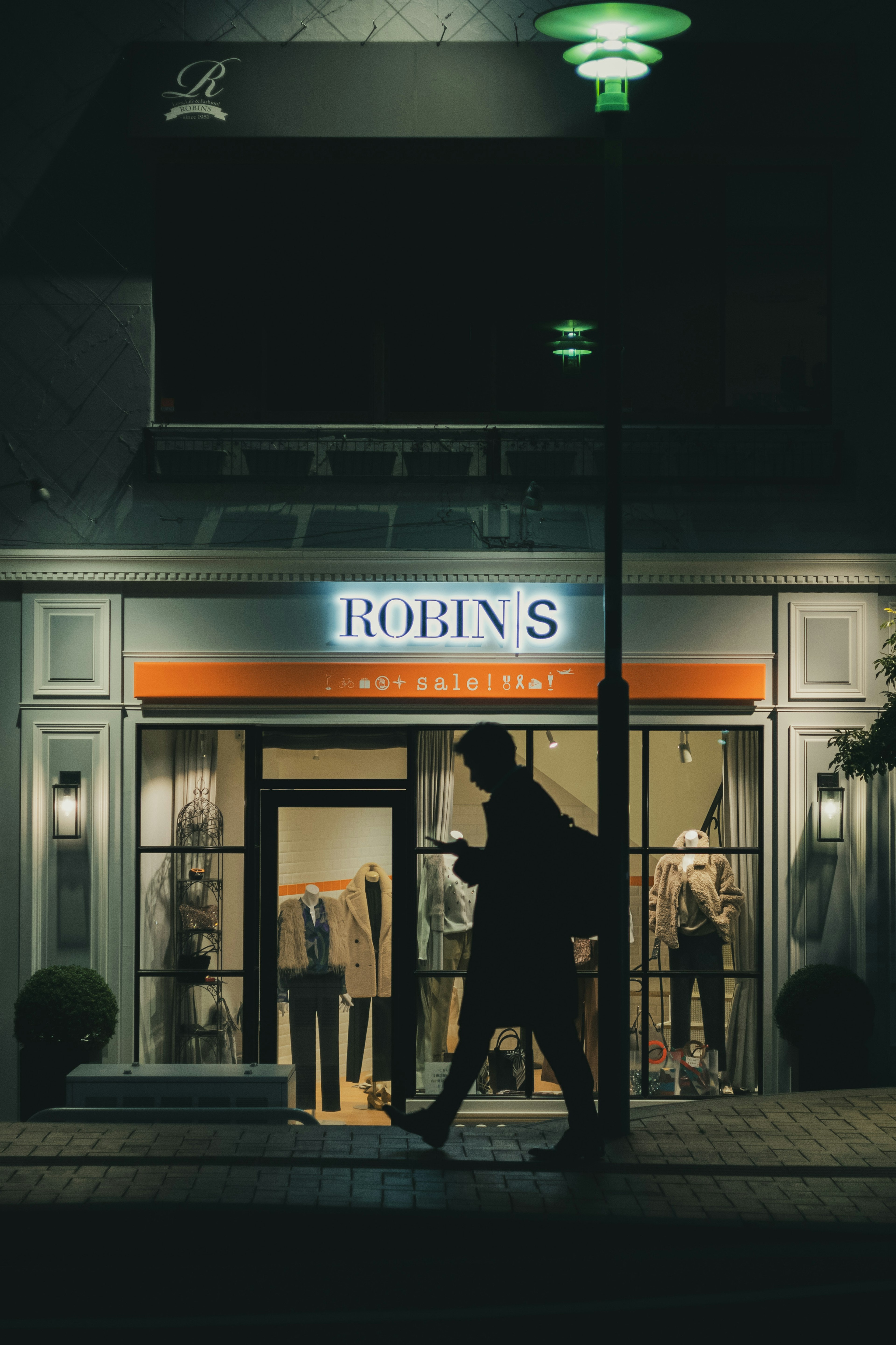 Escena nocturna de la tienda Robin's iluminada con un transeúnte caminando