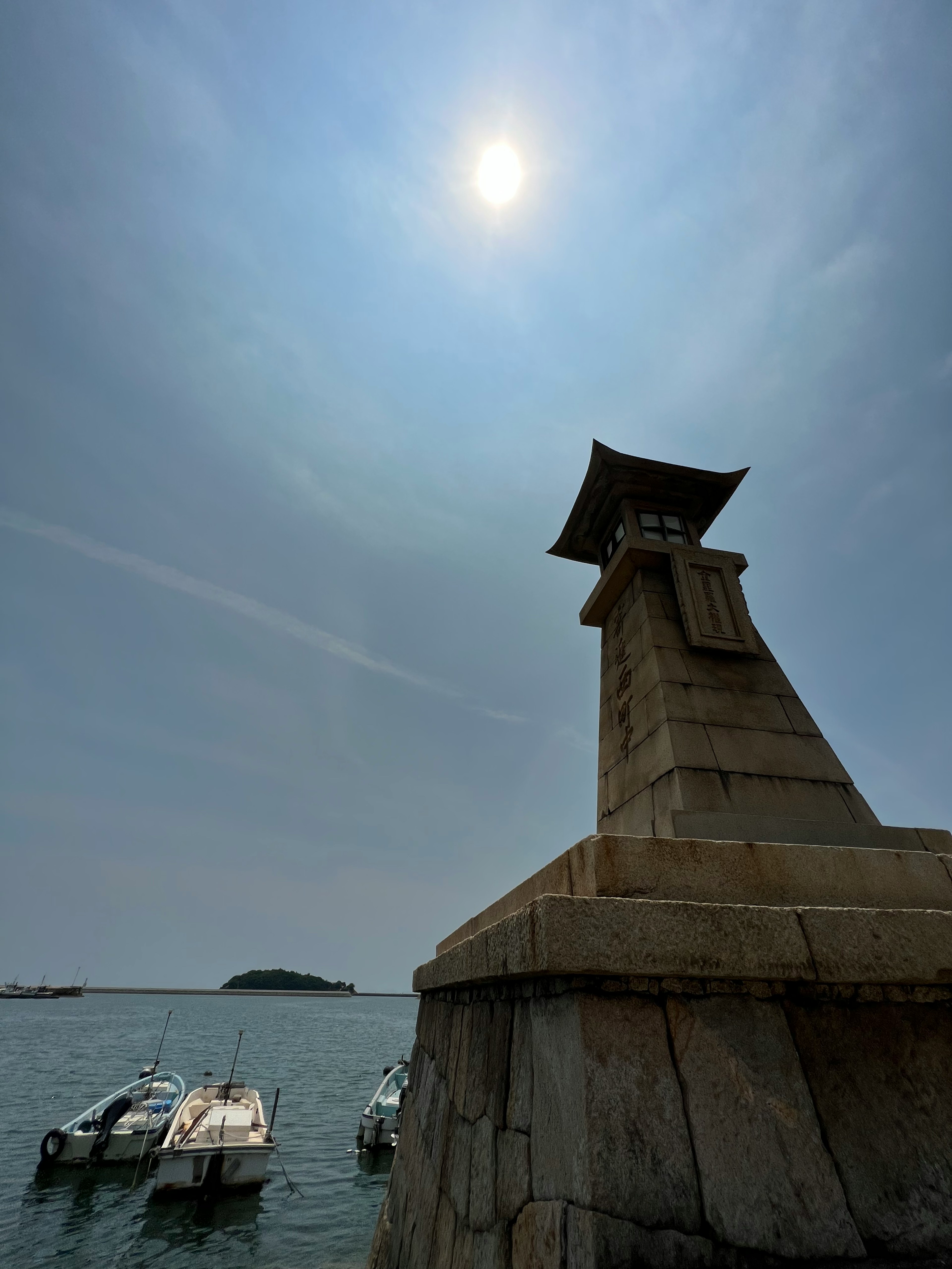 Vue pittoresque d'un phare au bord de la mer avec des bateaux au premier plan et un soleil éclatant dans le ciel