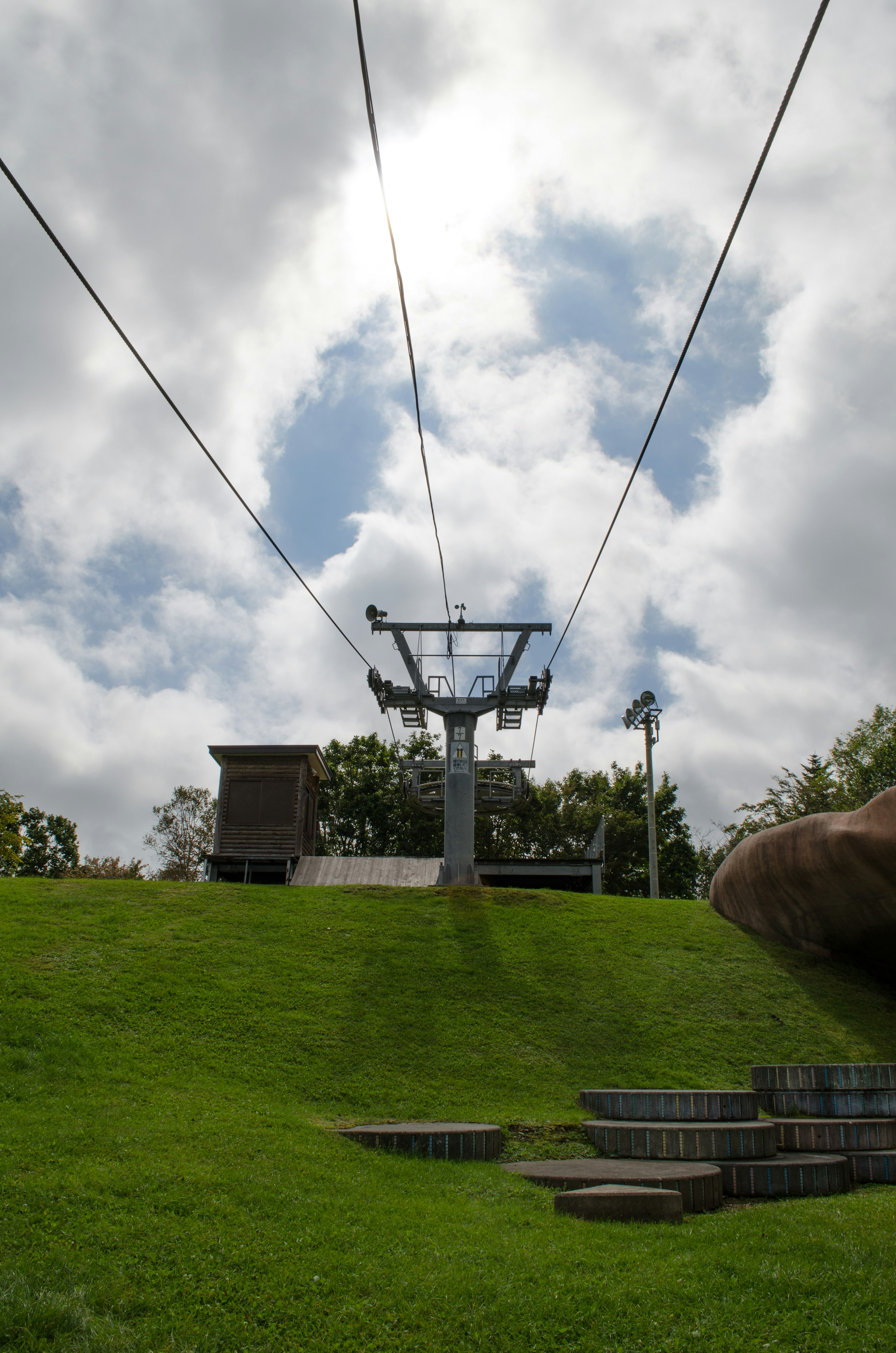 Cable car tower against a backdrop of clouds and blue sky with green grass