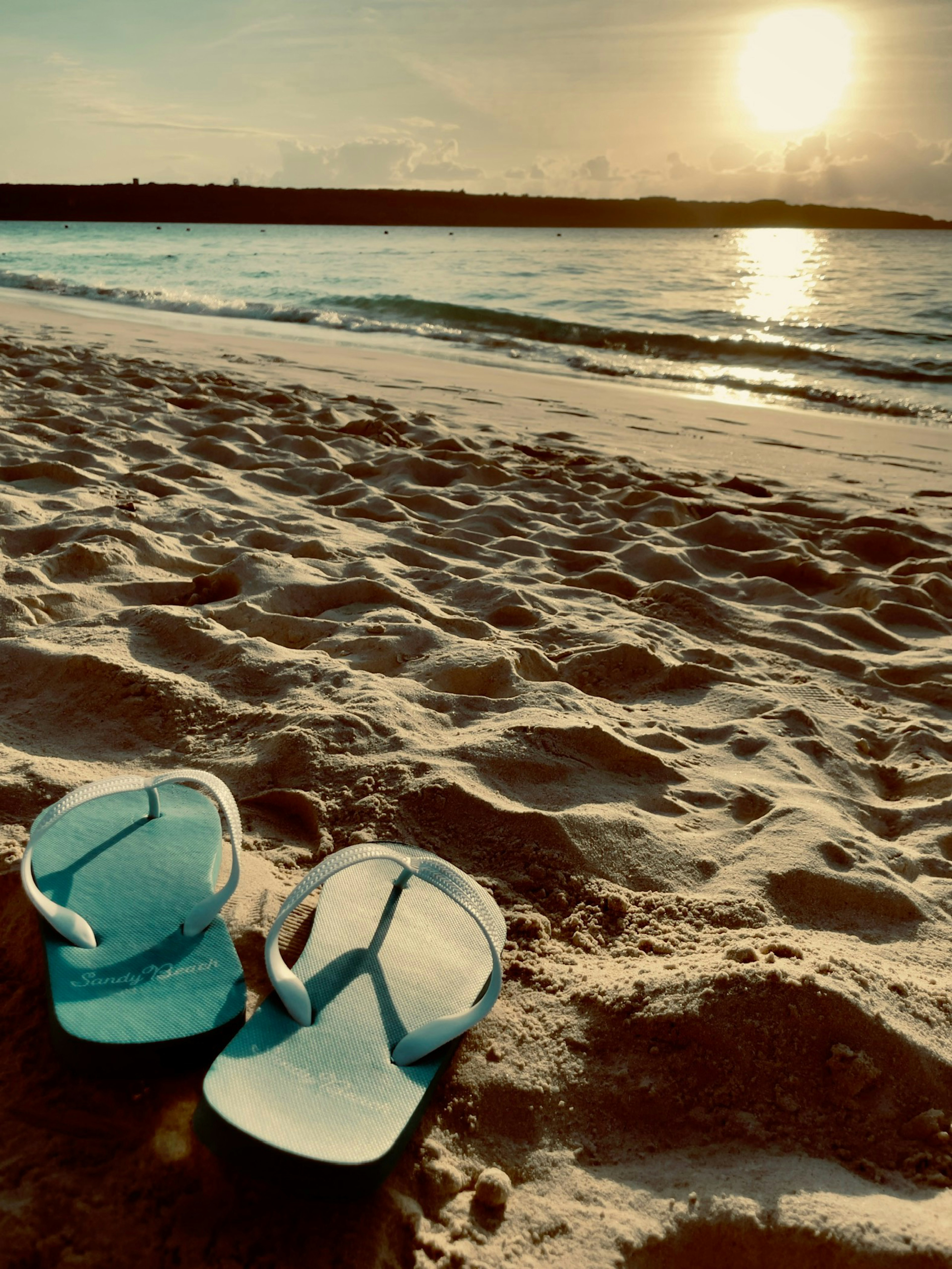 Blue flip flops on the beach at sunset