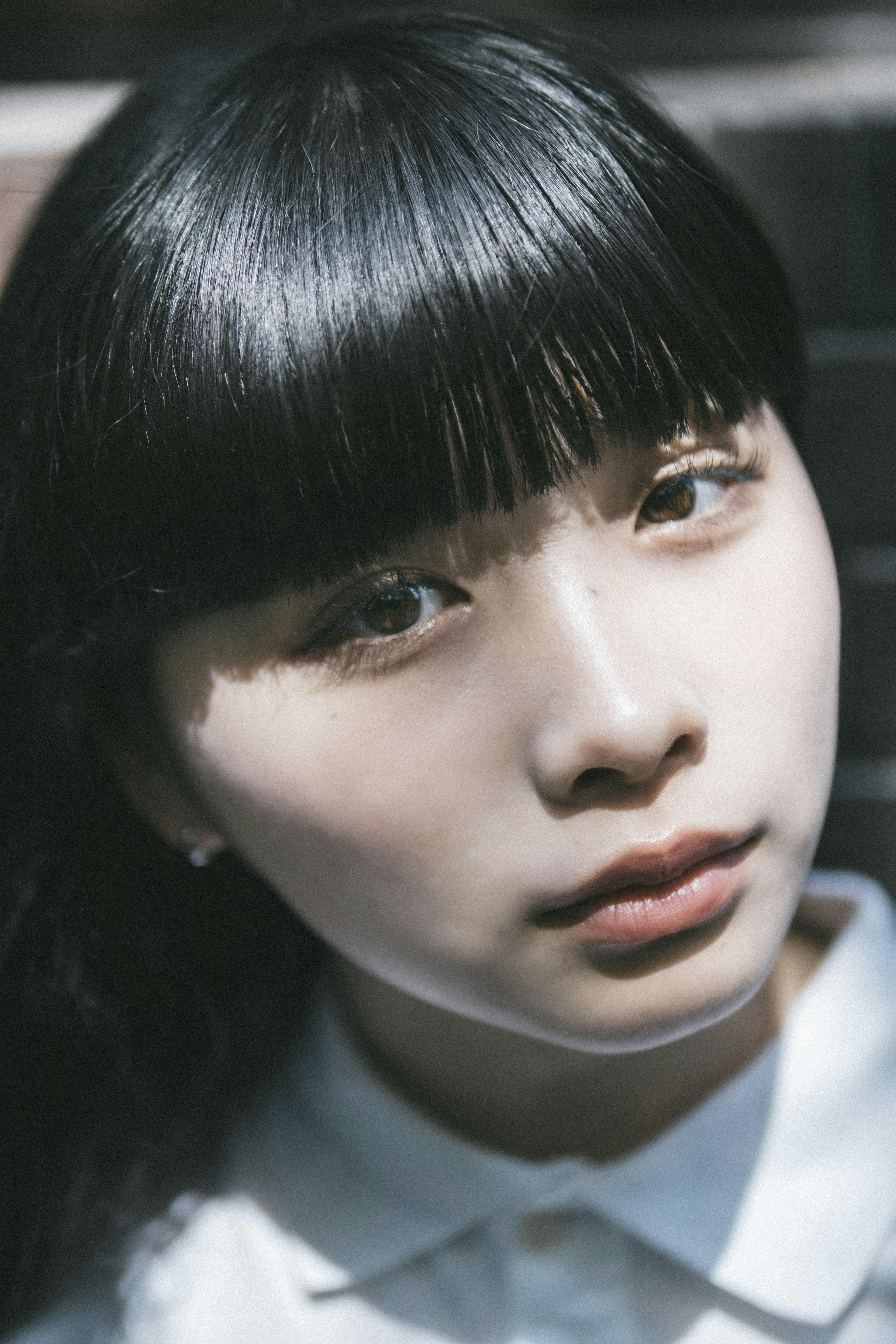 Portrait of a young woman with black hair and bangs wearing a white shirt against a bright background