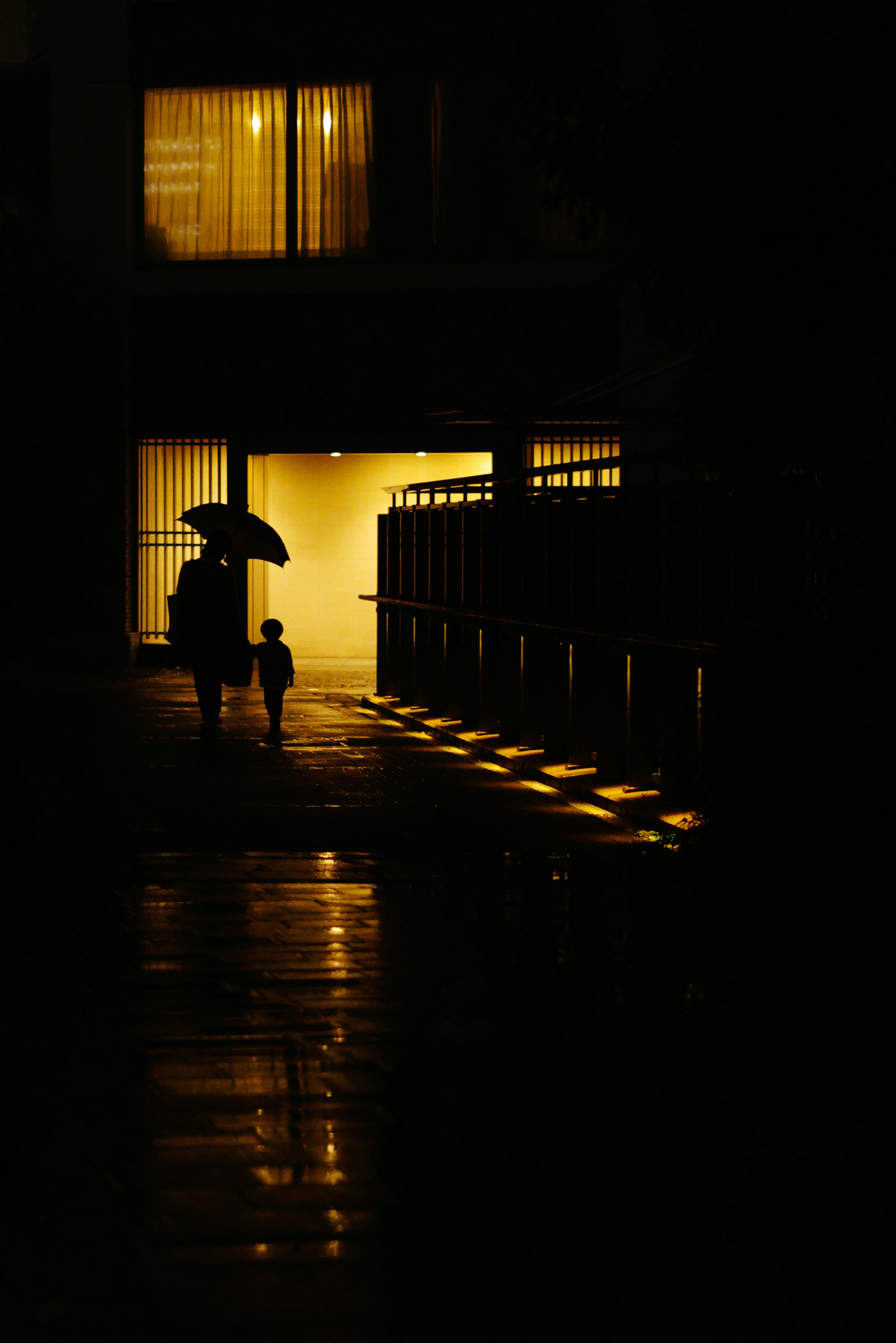 Silhouette of a parent and child walking in a dark street with bright window light