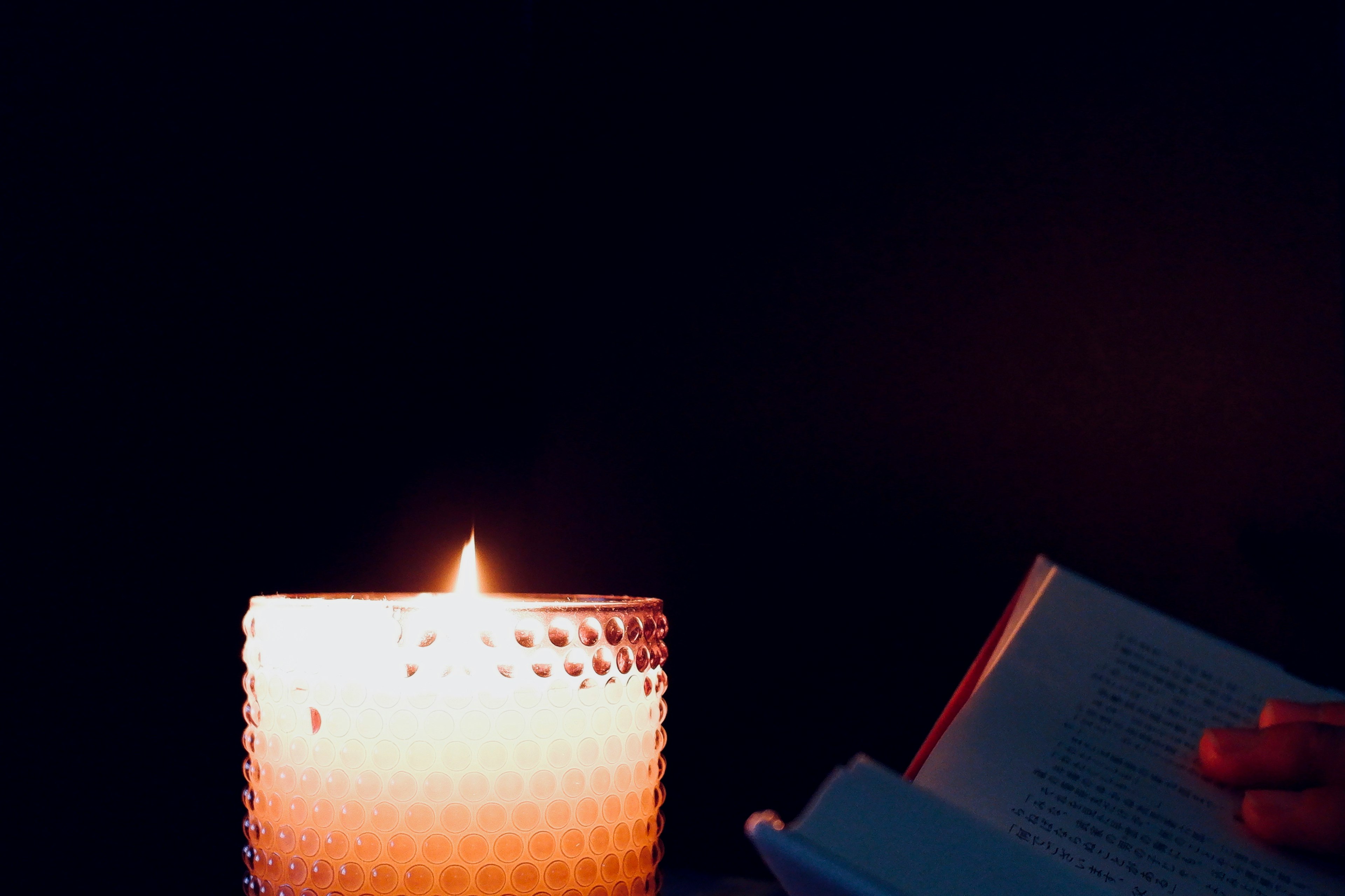 Una vela brillante y una mano sosteniendo un libro en un fondo oscuro