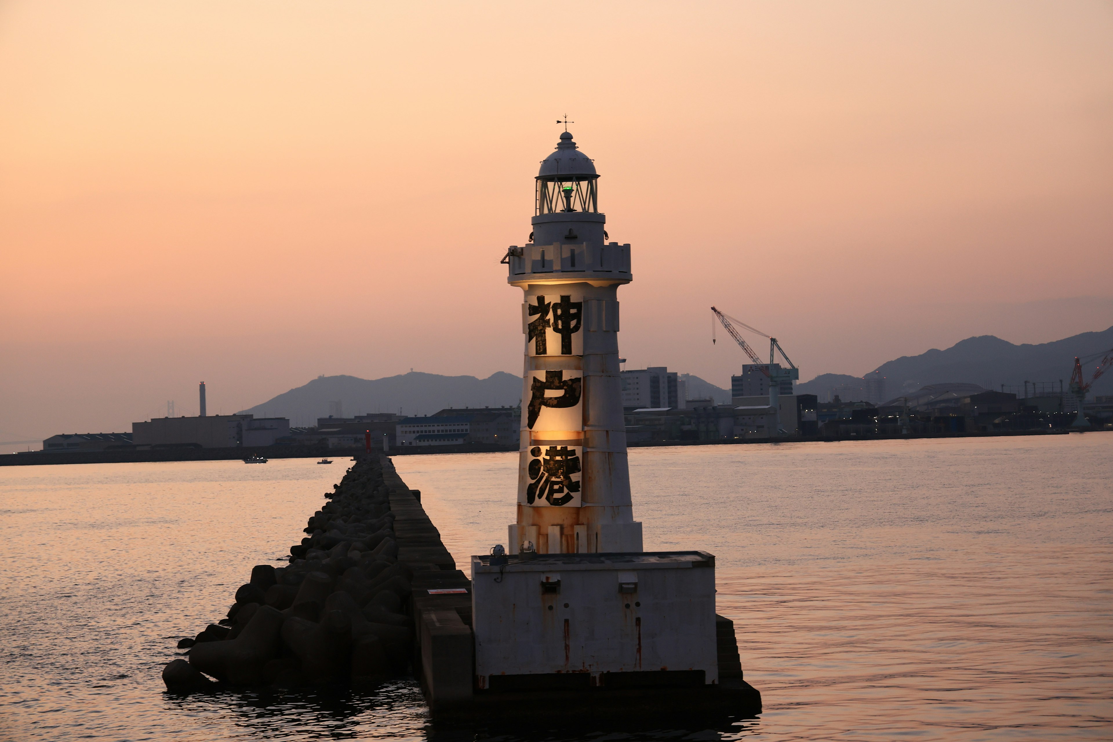 Leuchtturm steht im Sonnenuntergang mit umliegendem Wellenbrecher