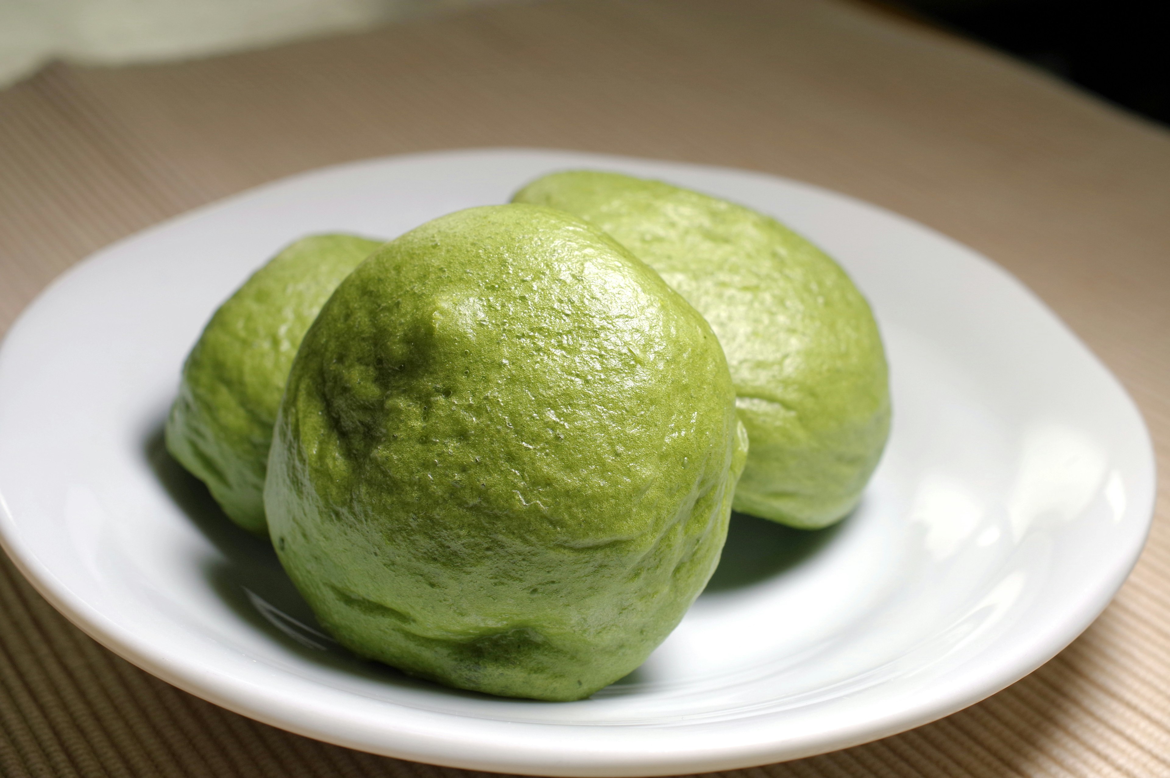 Three green steamed buns on a white plate