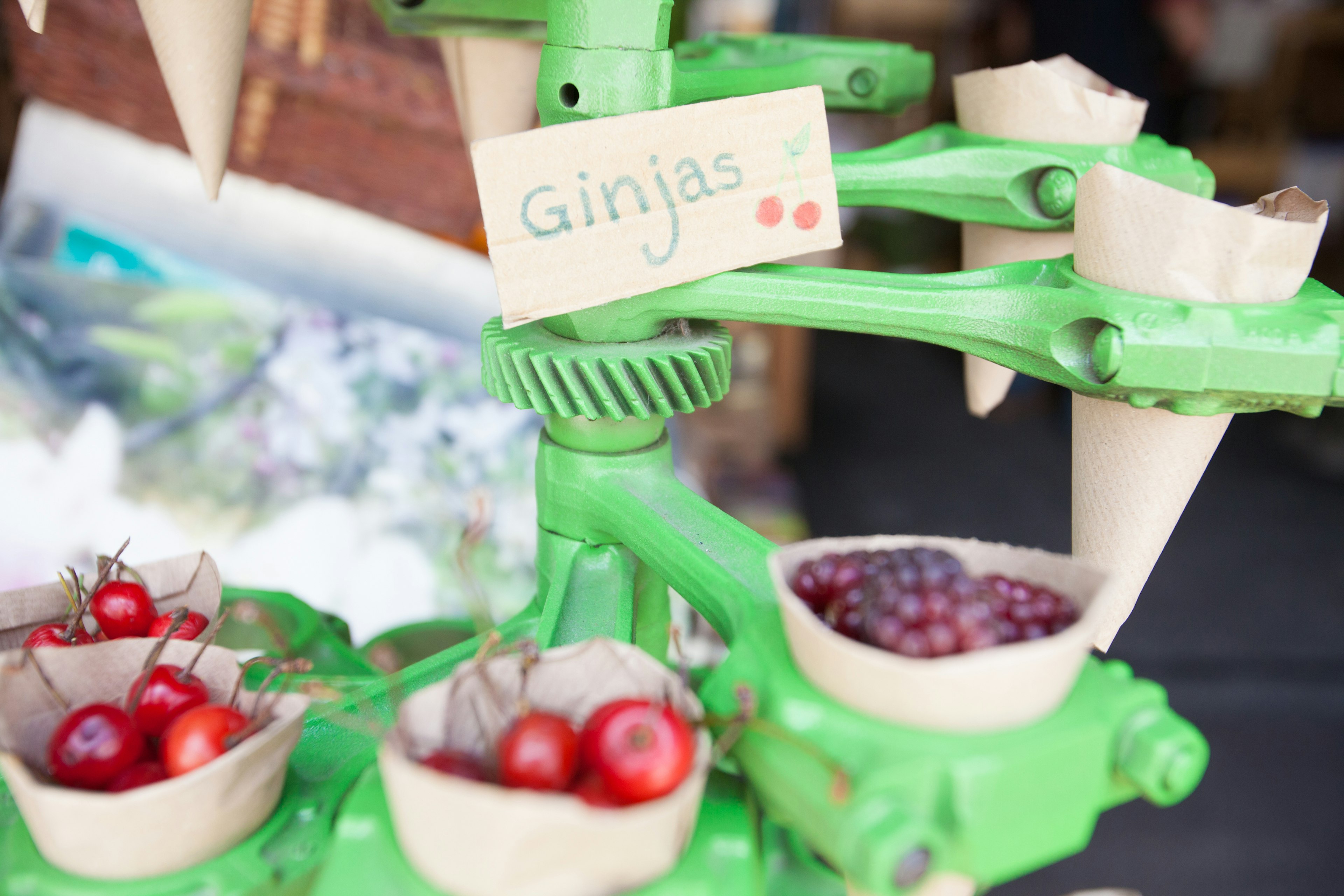 Green fruit stand displaying small cups with cherries and grapes