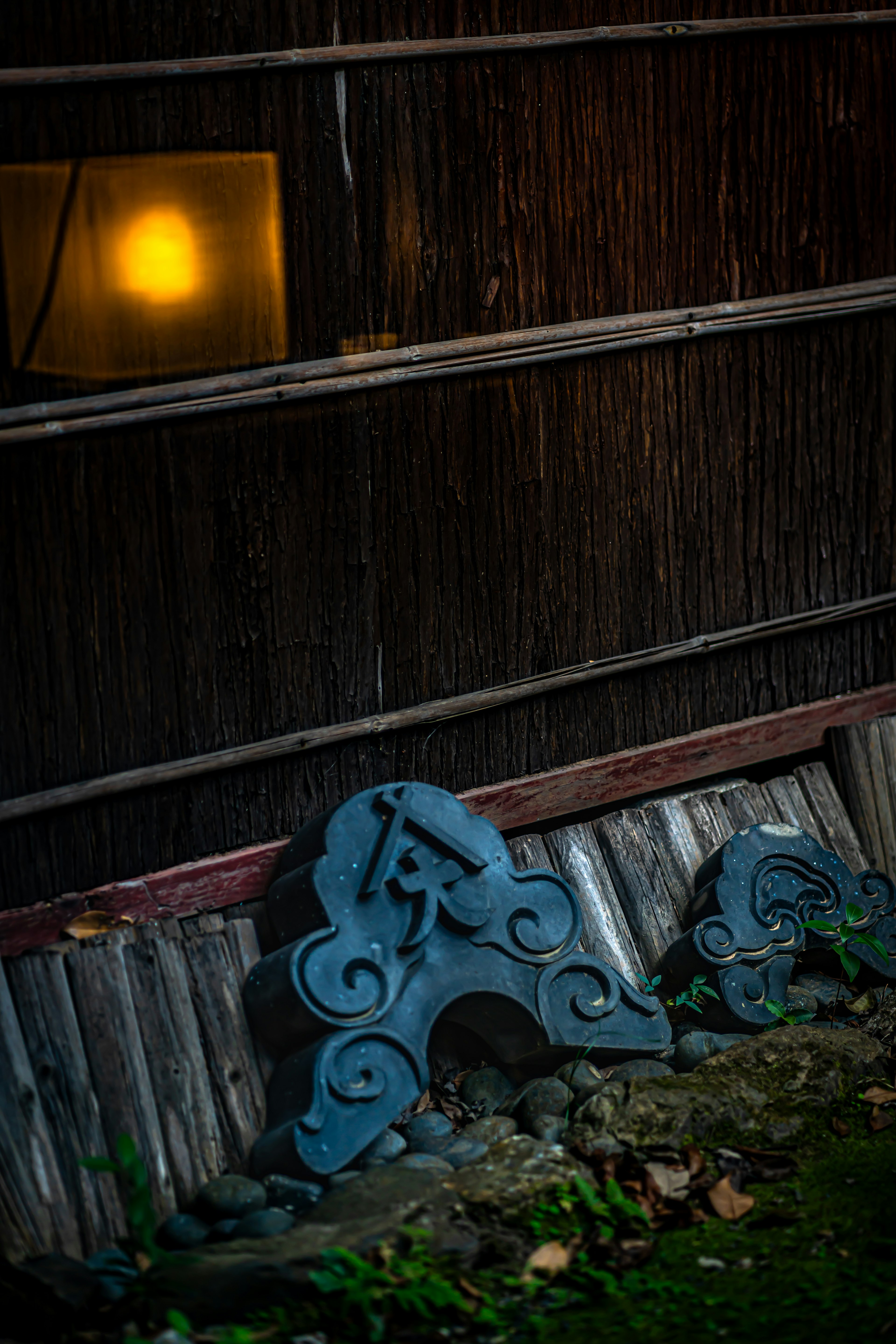 Japanese lantern glowing softly against a dark bamboo backdrop with blue decorative stones