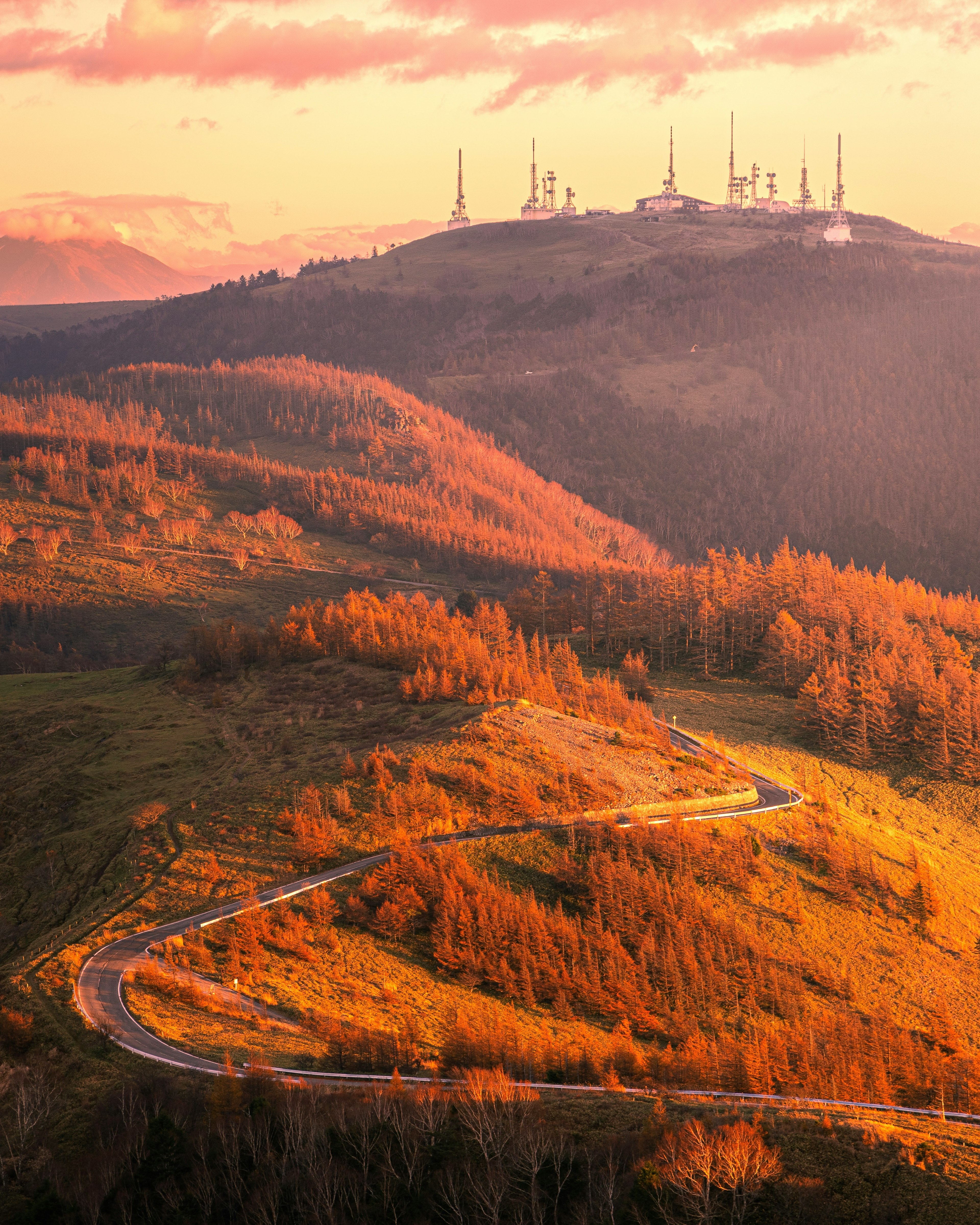 Route sinueuse à travers un paysage d'automne avec des tours de communication sur la colline