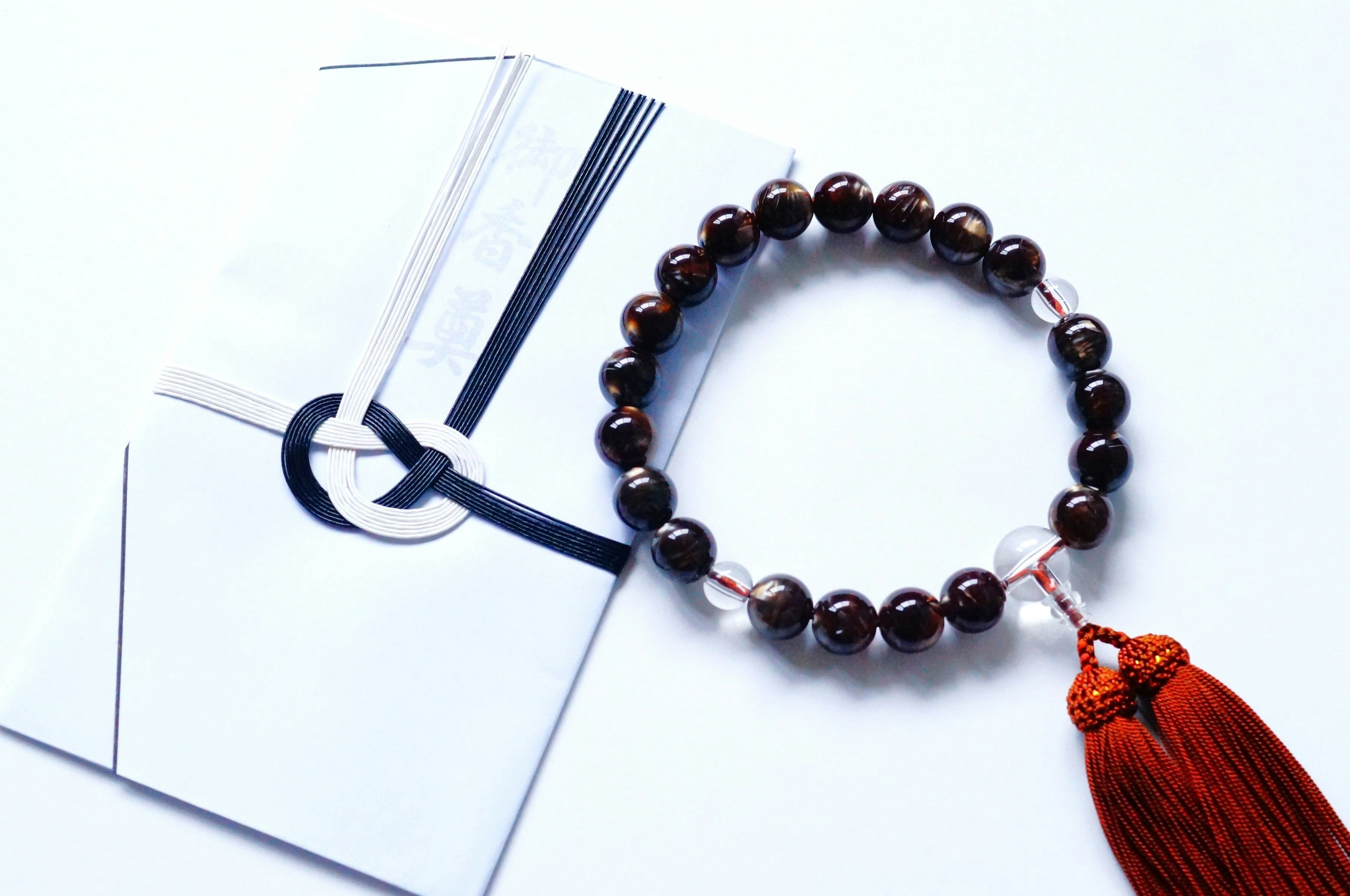 Bracelet de perles marron posé sur une enveloppe blanche avec un gland rouge