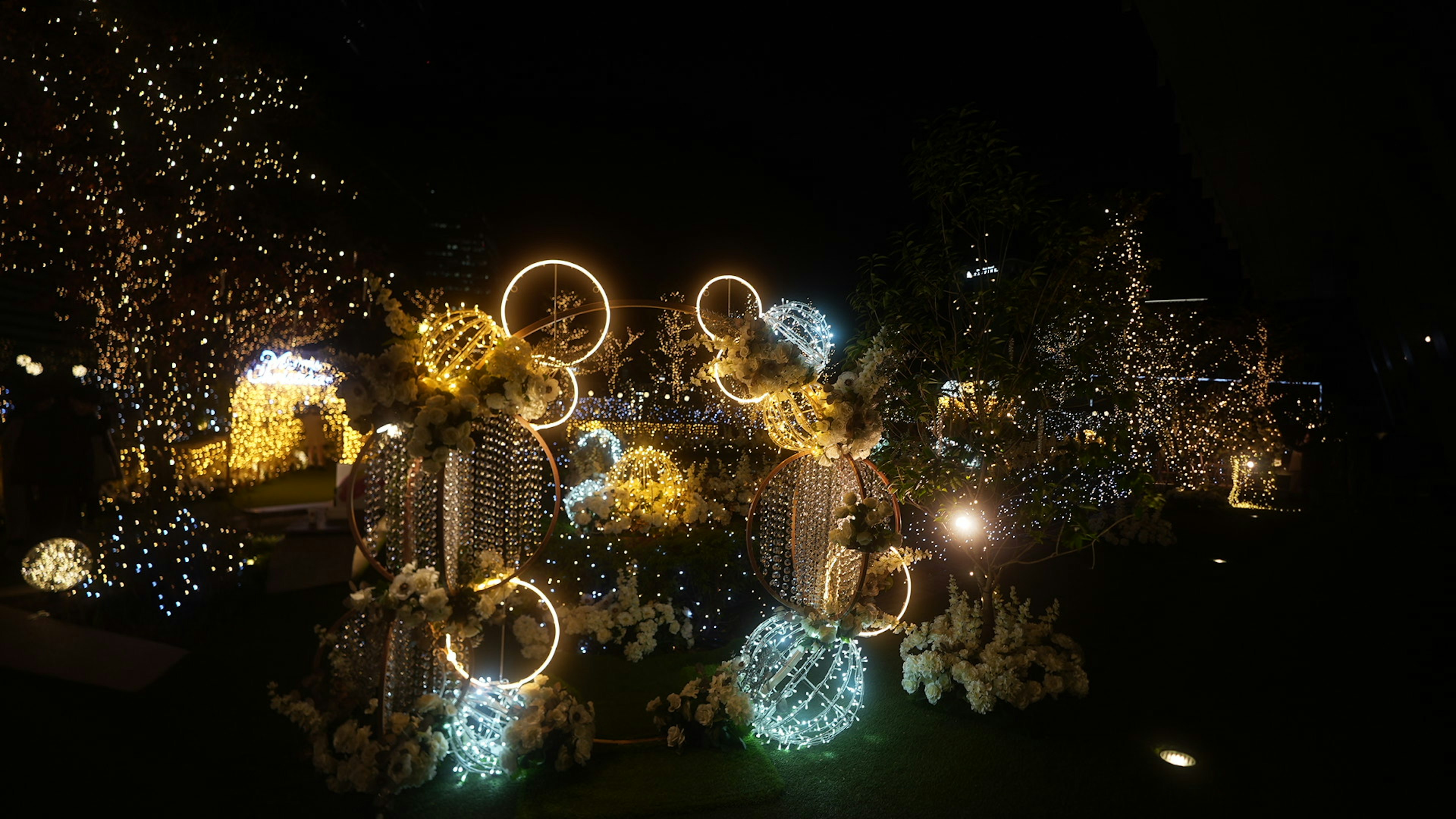 Beautiful garden scene decorated with lights at night featuring glowing ornaments and colorful lights