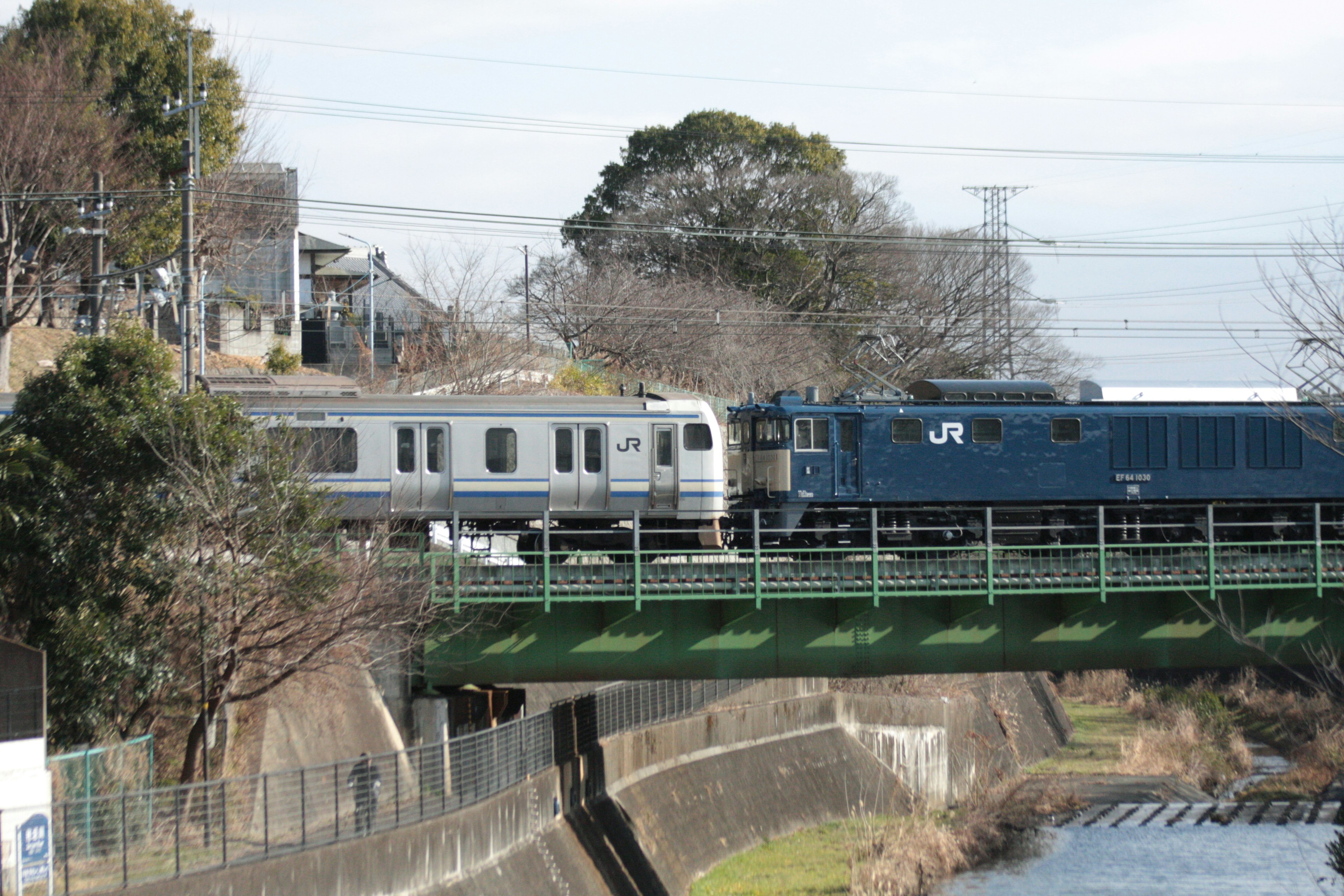 A train crossing a bridge featuring a blue locomotive and a silver passenger car